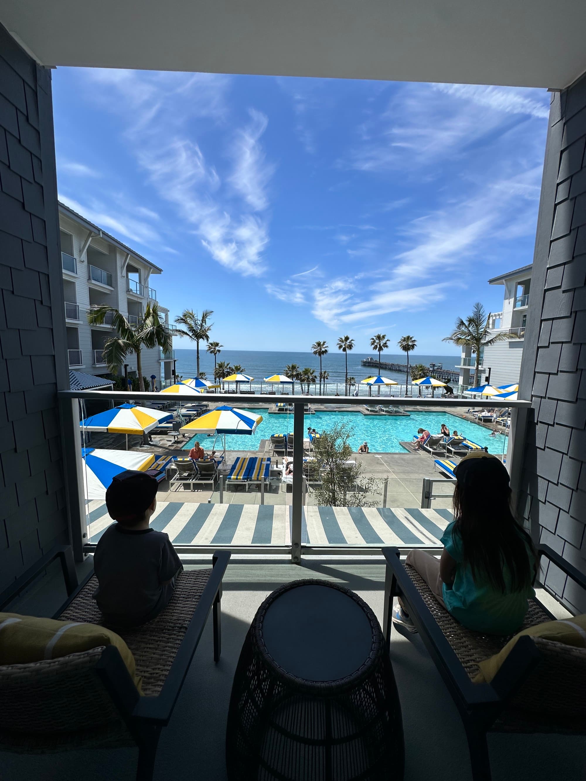 Two children on a balcony overlooking a hotel pool area during the daytime