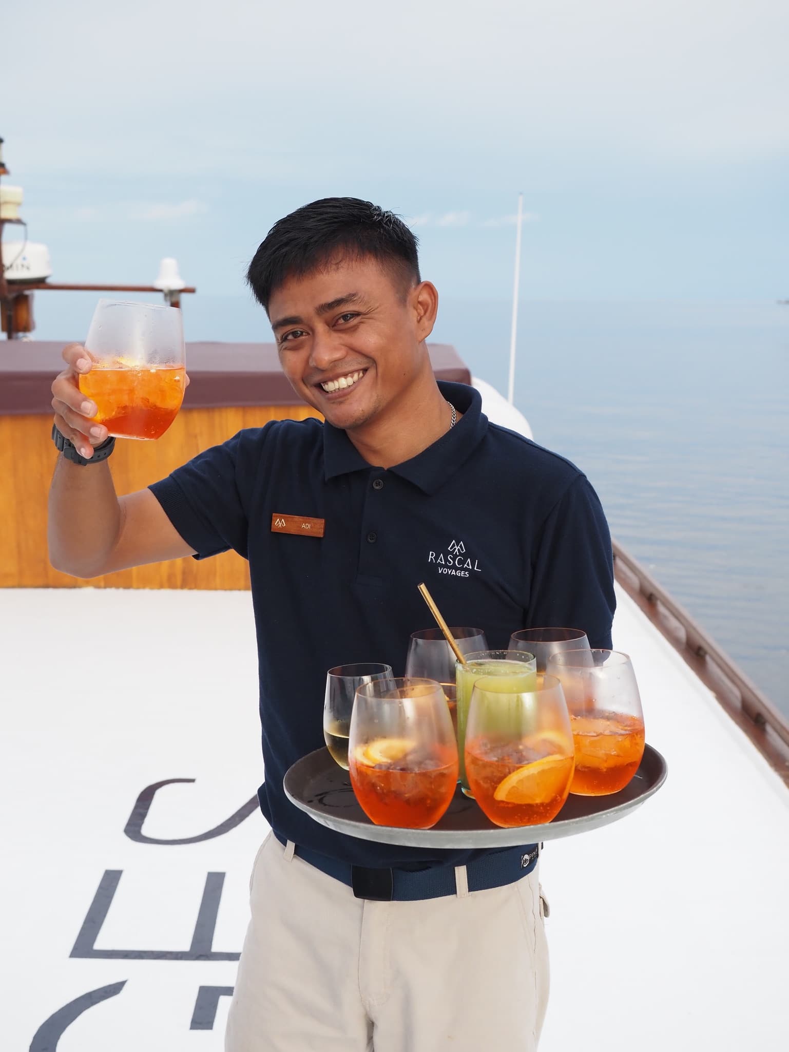 A server holding a dray of orange drinks in stemless glasses on a boat deck