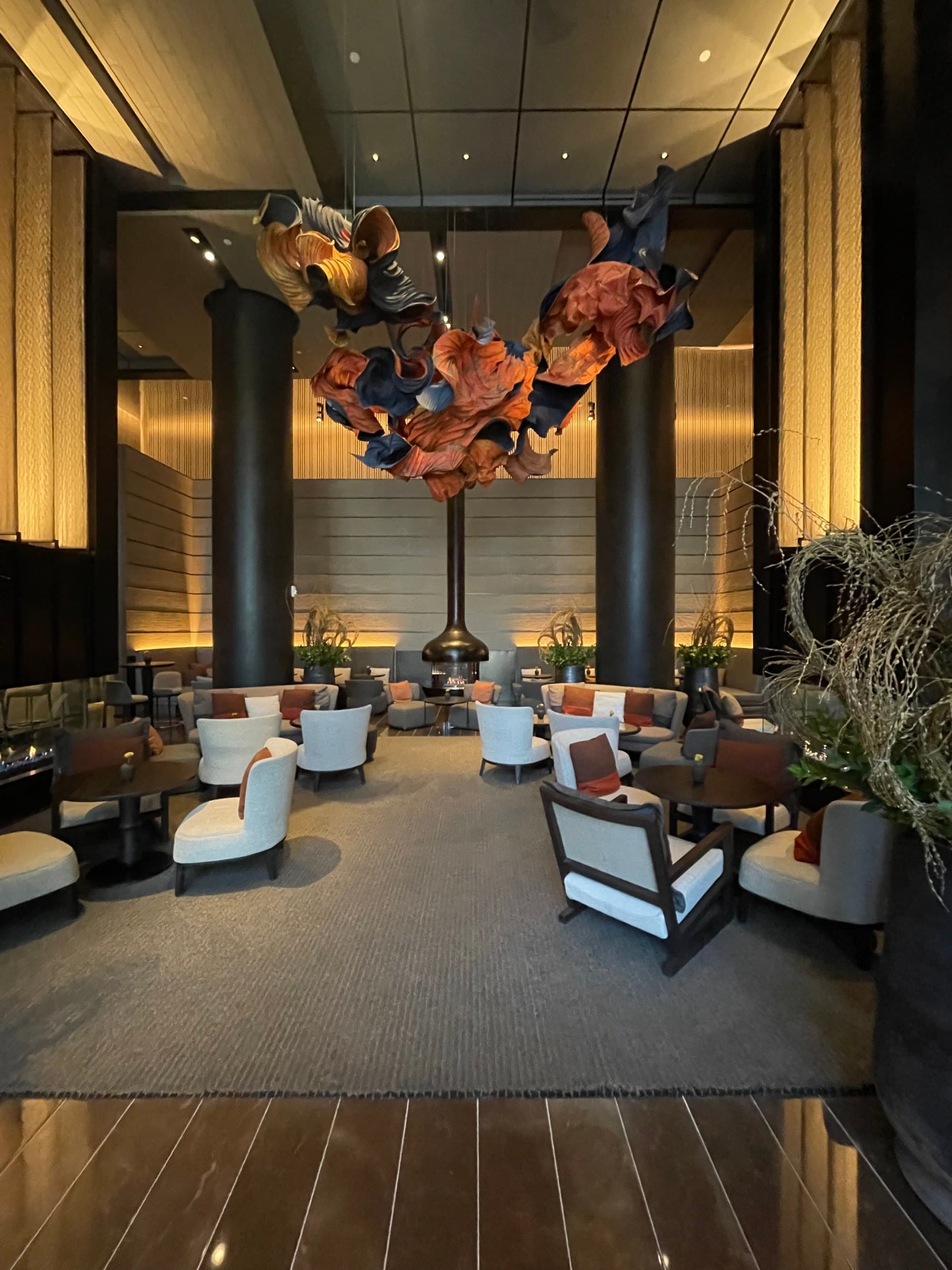 Inside one of the hotel's social spaces, with comfy chairs, small, round tables, a hanging, abstract sculpture, high ceilings and grand columns.