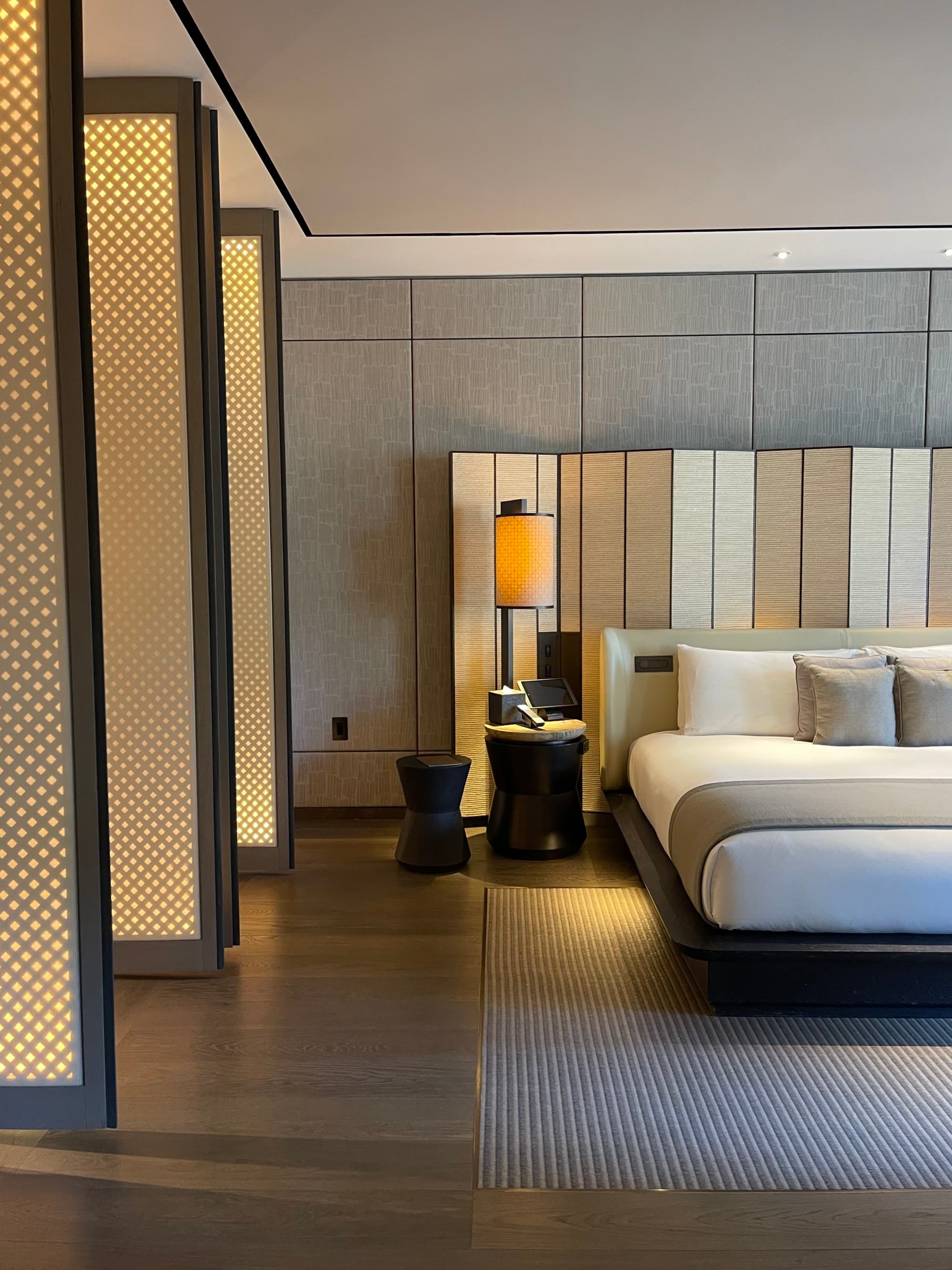 Inside one of the hotel's room, with a large white and beige bed and modern decor.