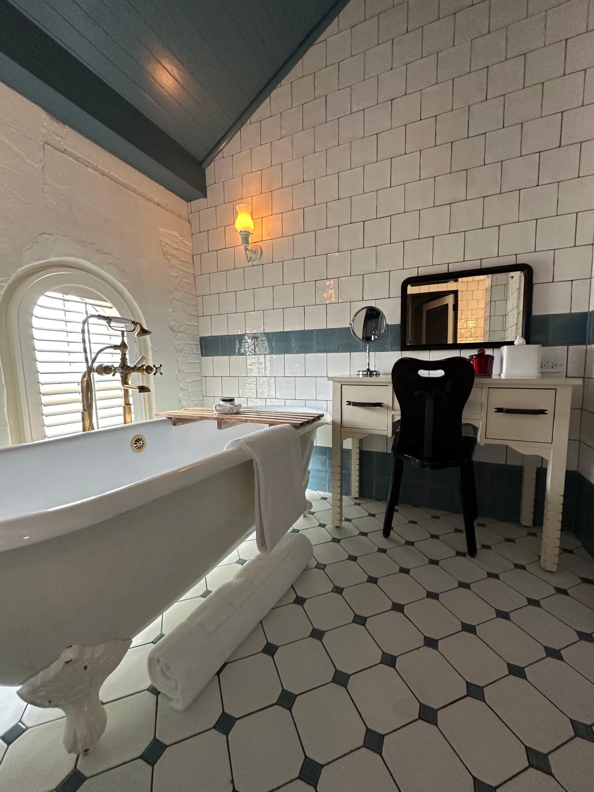 A white and black tiled bathroom with a white clawfoot tub and a vanity desk behind it.