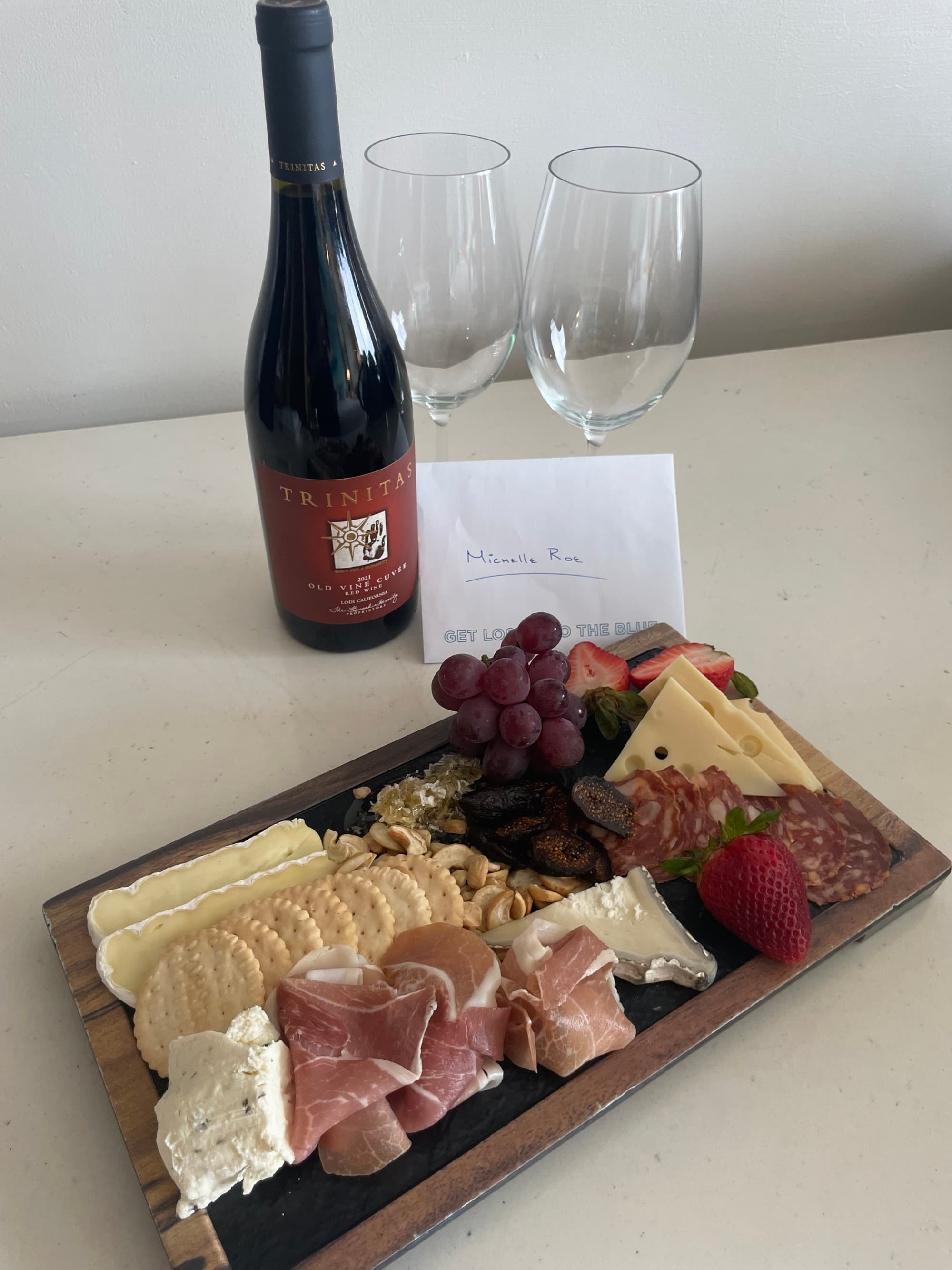 A tray of charcuterie next to a bottle of Trinitas wine, two glasses and a welcome note - Michelle Roe