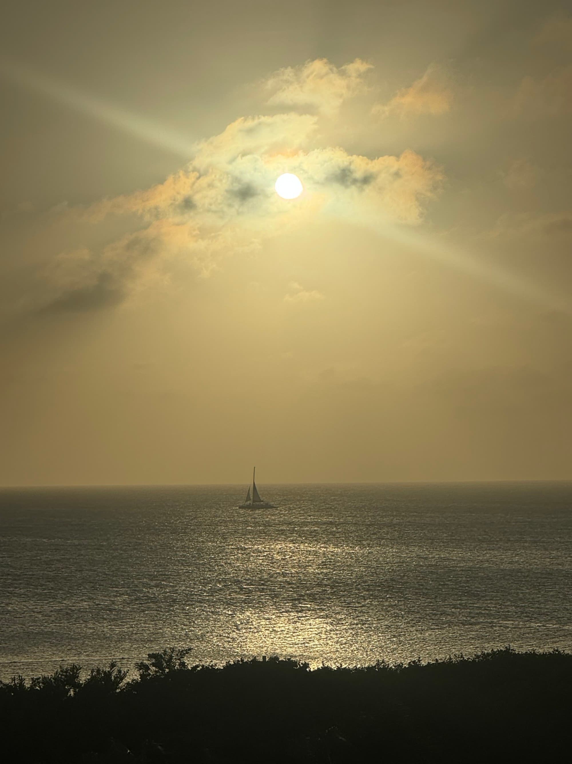 RView of the ocean with a boat in the distance with the sun shining through the clouds