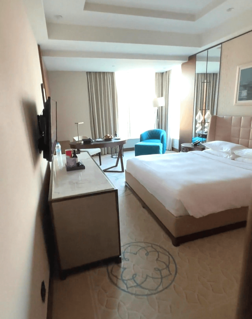 A hotel room with a bed in the middle and a blue chair in the corner