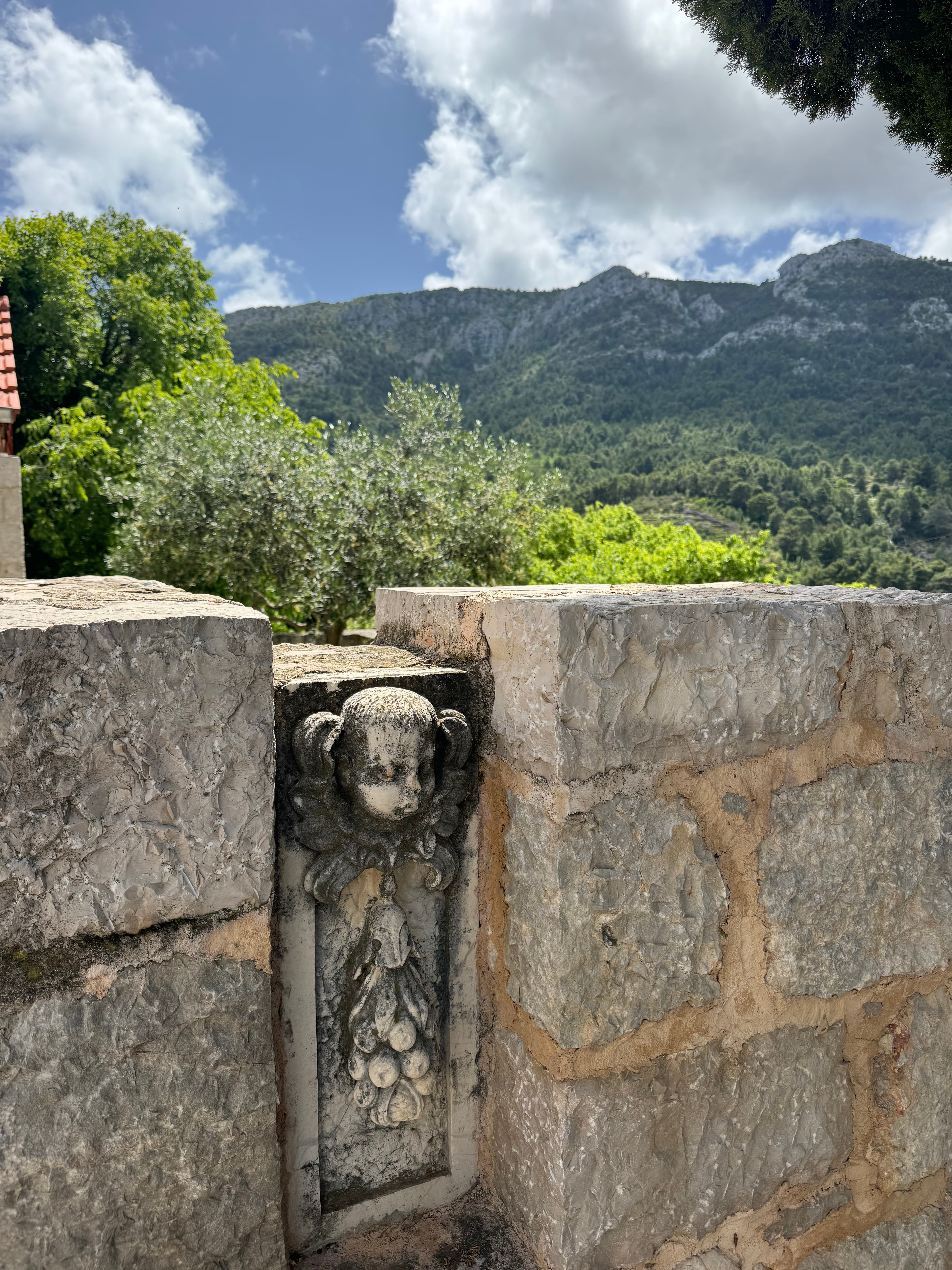 A view of an old stone wall with an engraved head in the middle, with mountains in view.