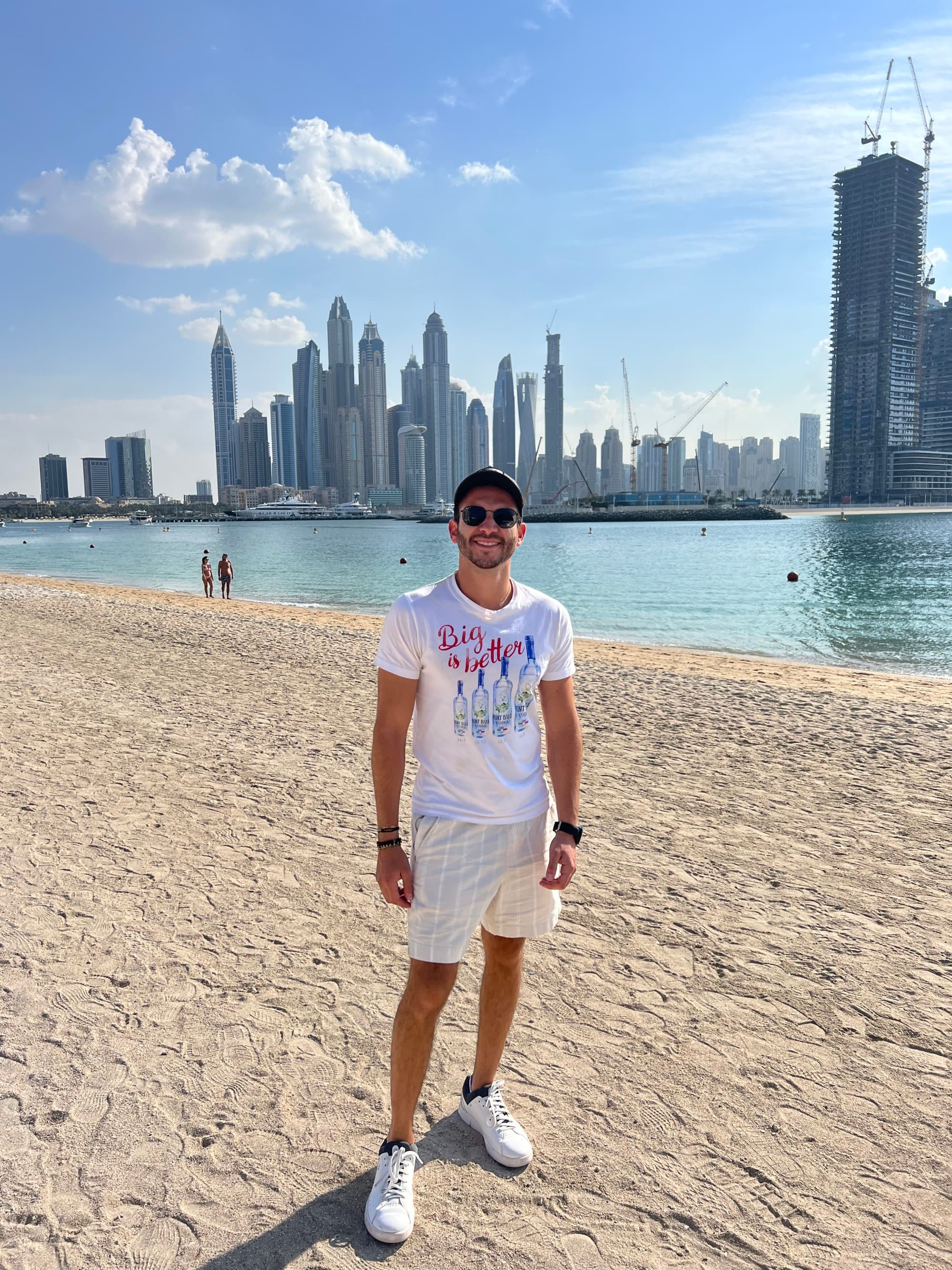 a man in a white shirt stands on a beach near a city