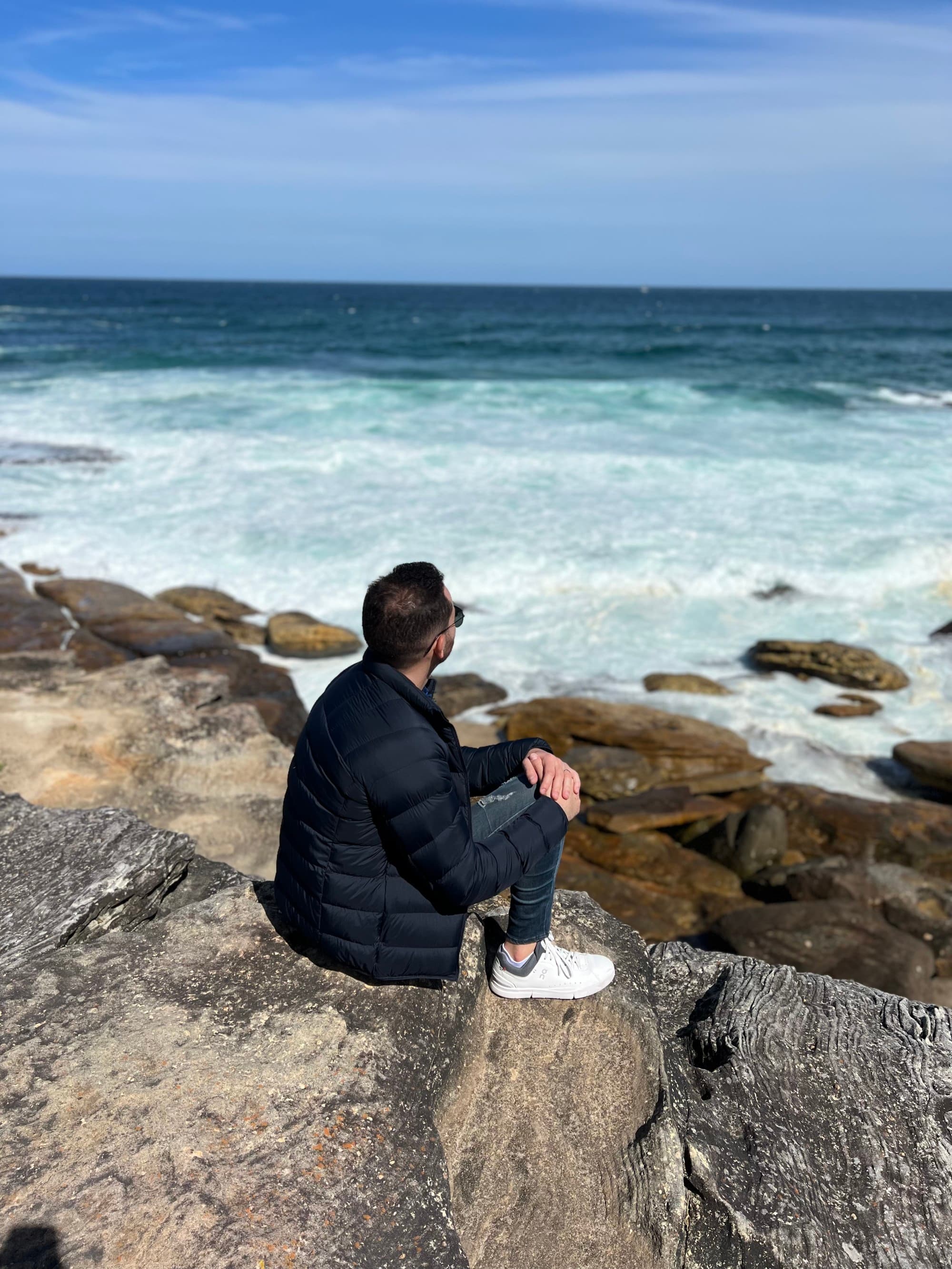 a man sits on a rock overlooking the sea