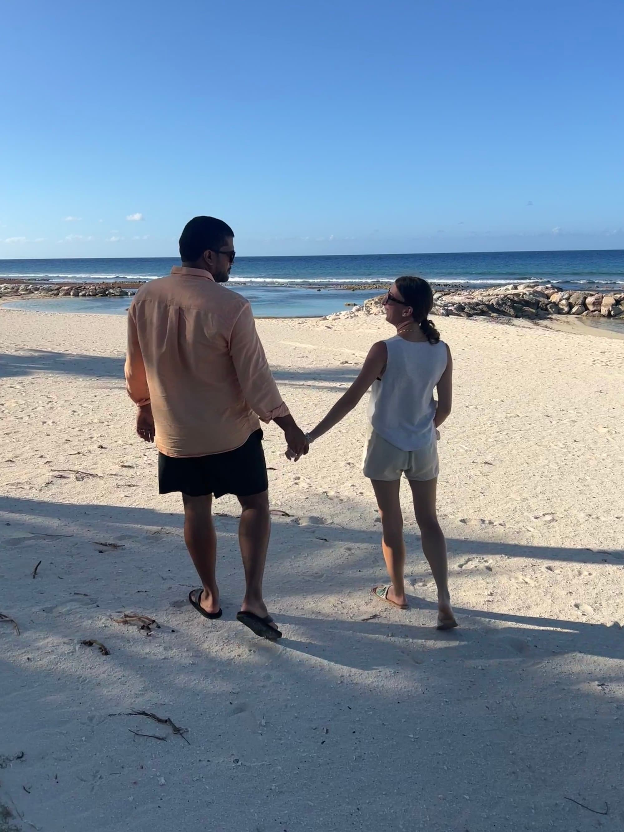 Couple holds hands while walking on the sand.