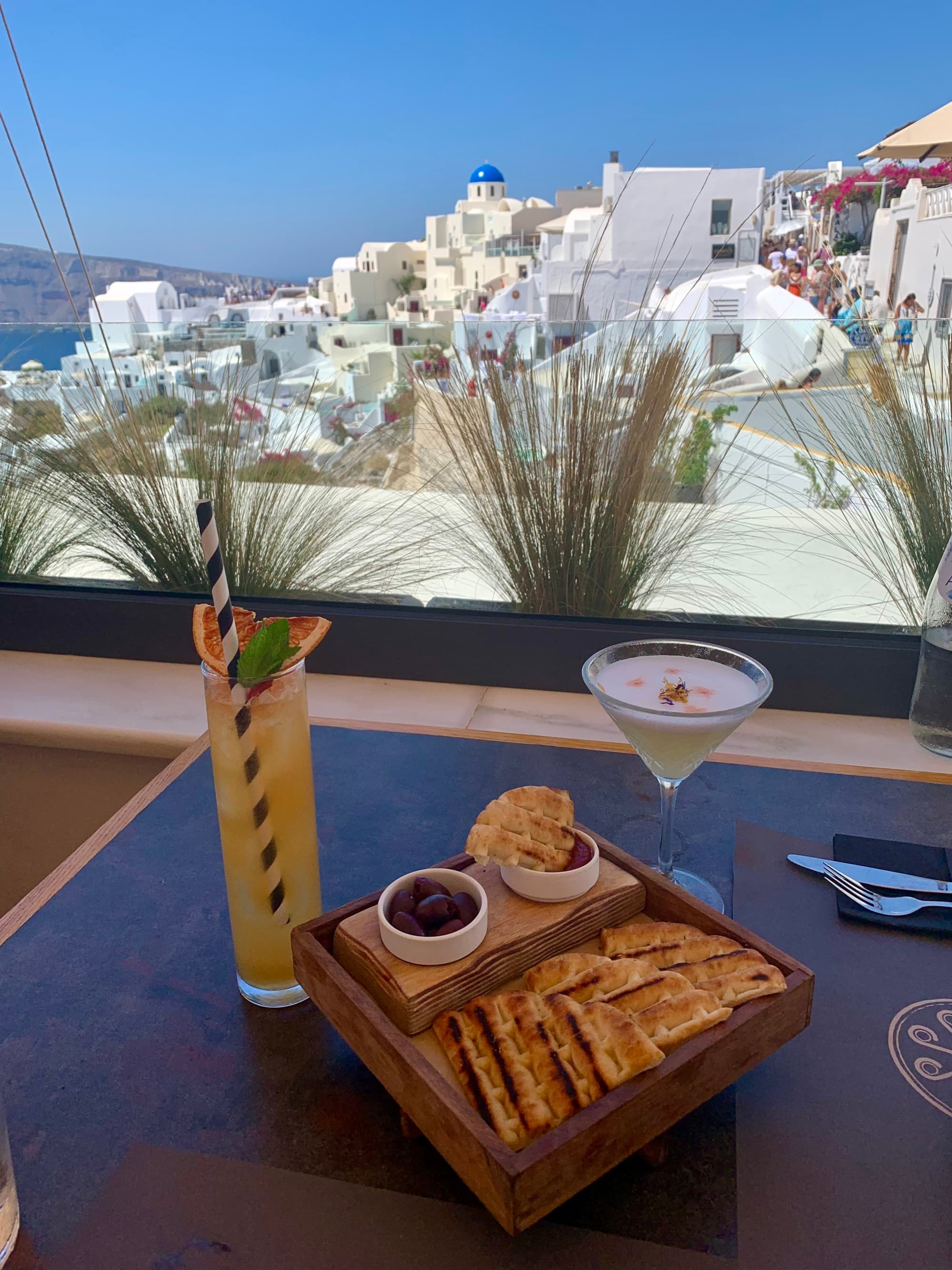 Cocktails and tapas on a table with whitewashed buildings in the background.