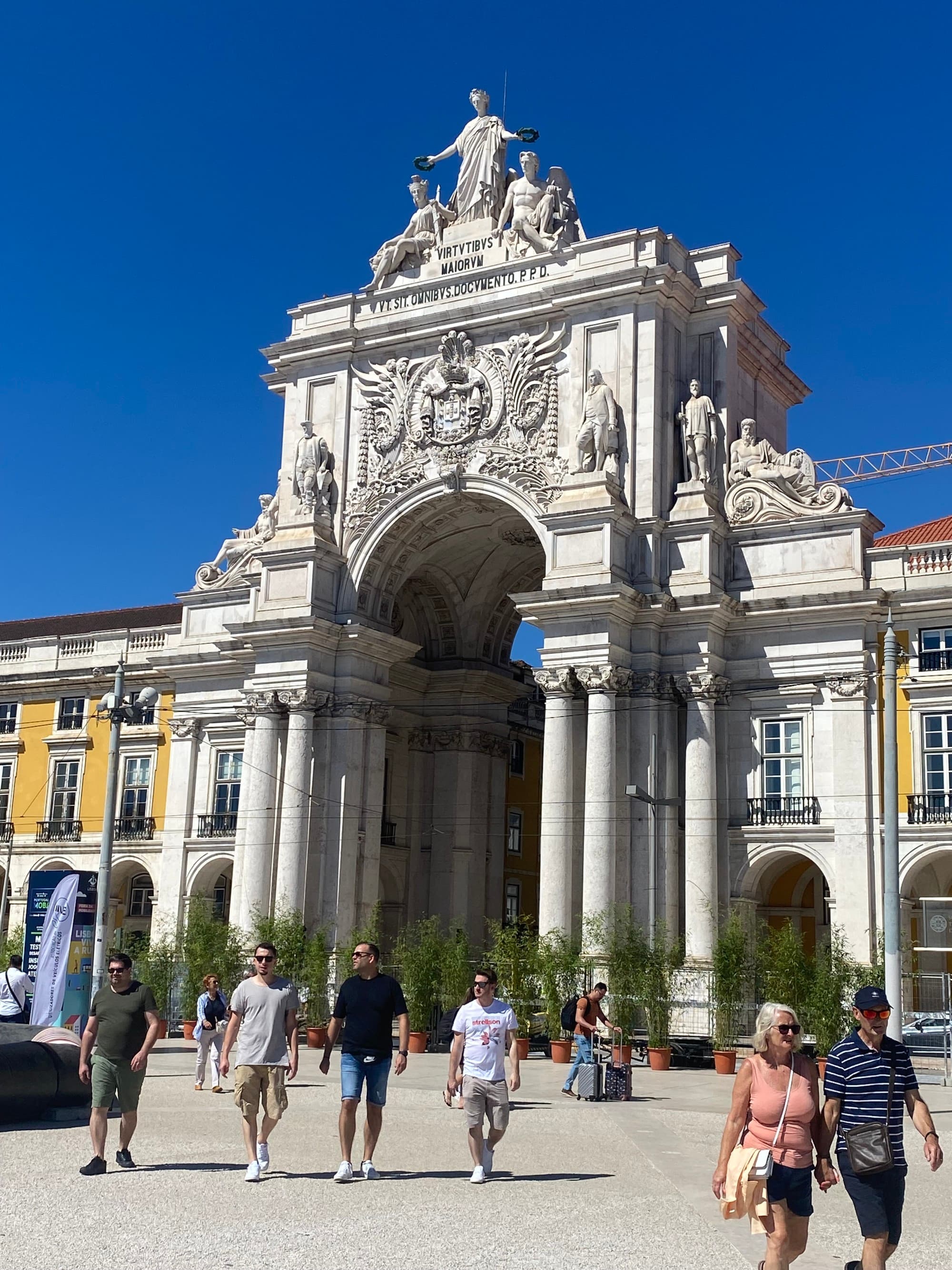 Historic arched building thronged by visitors on a sunny day.