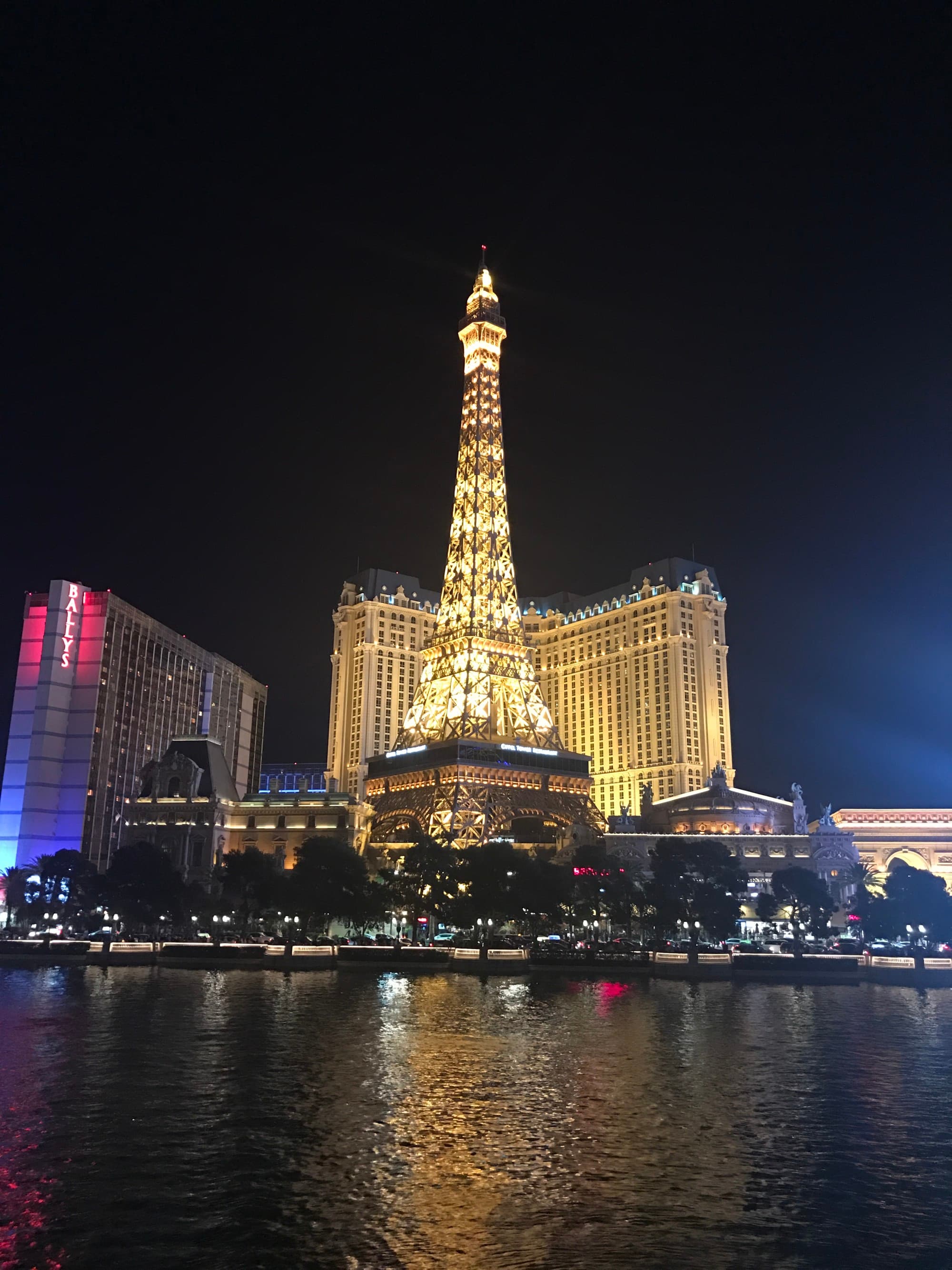 A view of the Paris Hotel in Las Vegas with its iconic Eiffel Tower structure, illuminated at night.