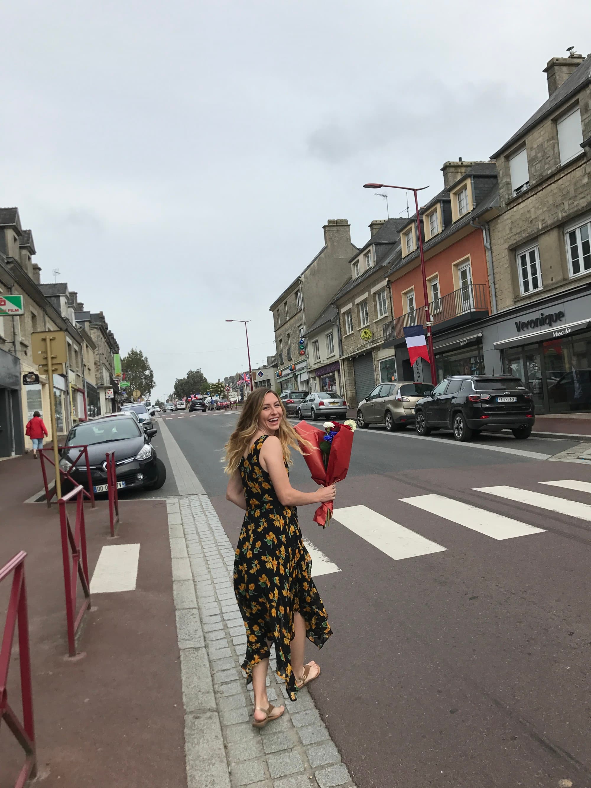 a woman in a dress holds a bouquet of flowers as she walks across the street