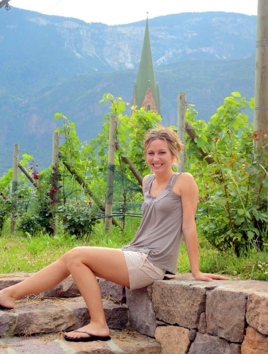 a woman sits on a stone ledge amid vineyards
