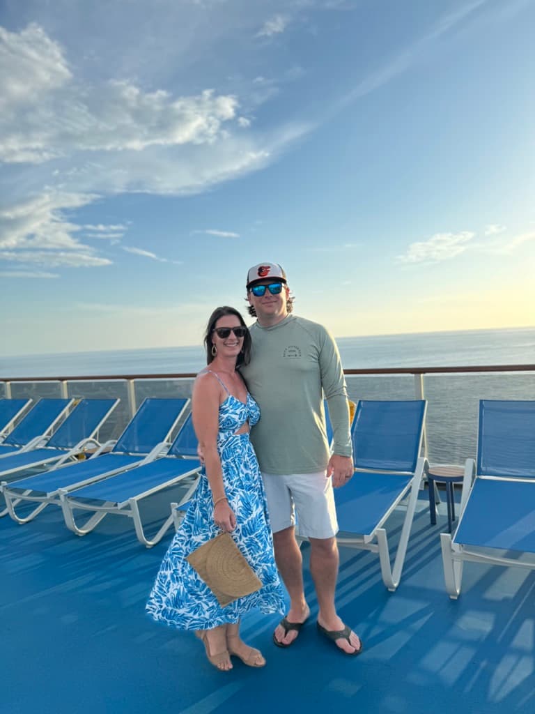 A couple posing together for a photo on a ship deck with pool chairs behind them