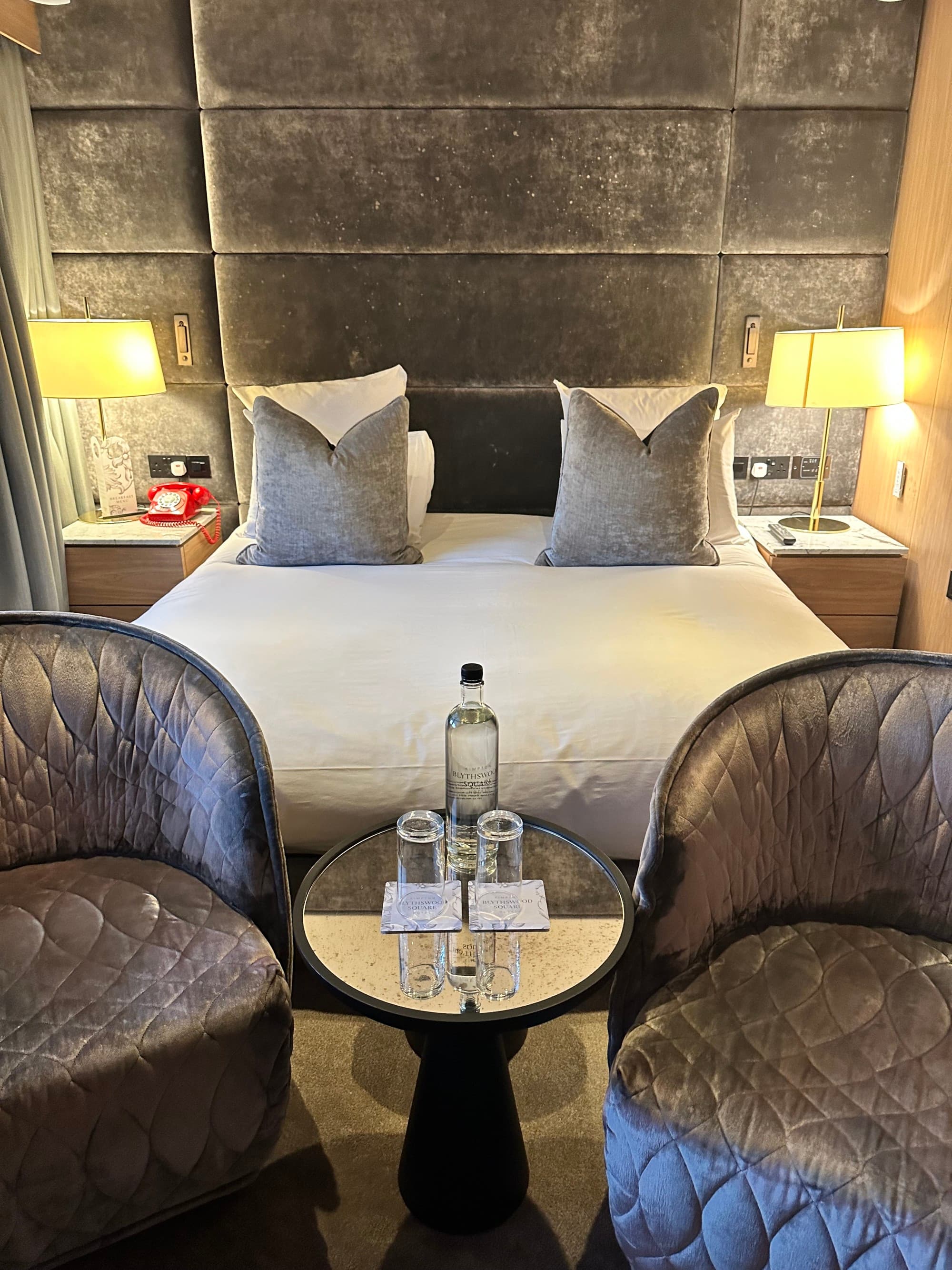 Hotel room with a bed with white linen and two leather conversation chairs.