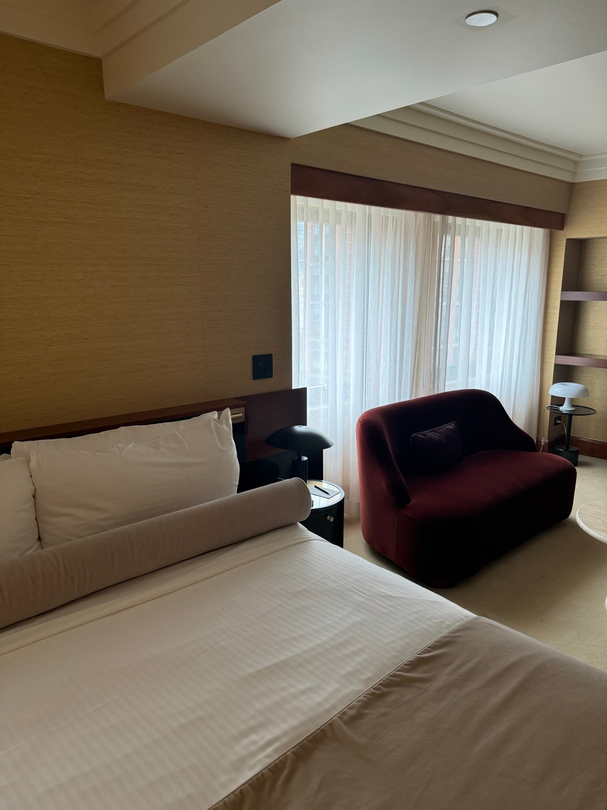 Hotel room with a serene interior and a large window with drapes.