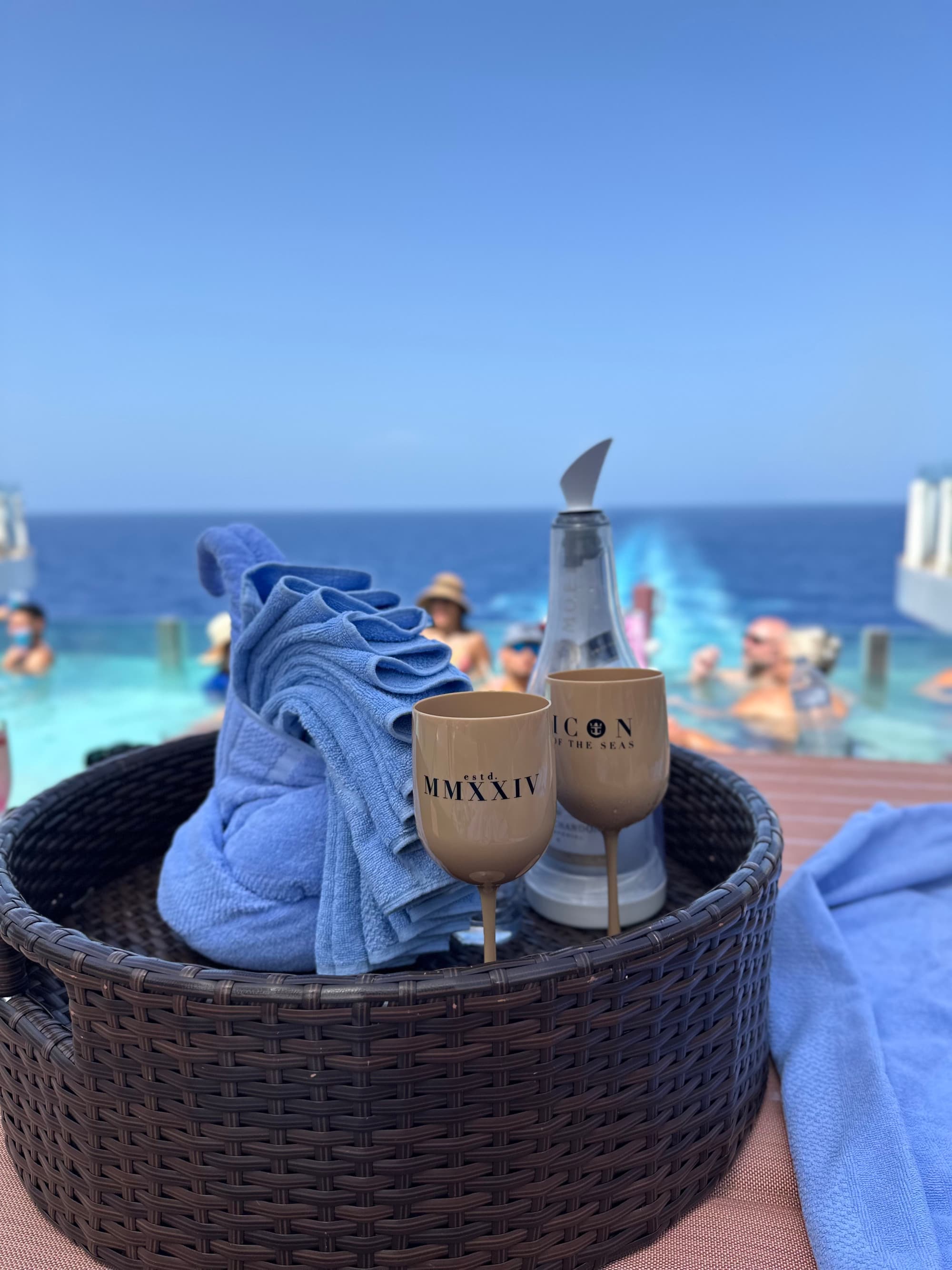 Hideaway adults-only infinity pool sits on deck with a basket of towels, beverages and other sunbathing amenities on a sunny day.