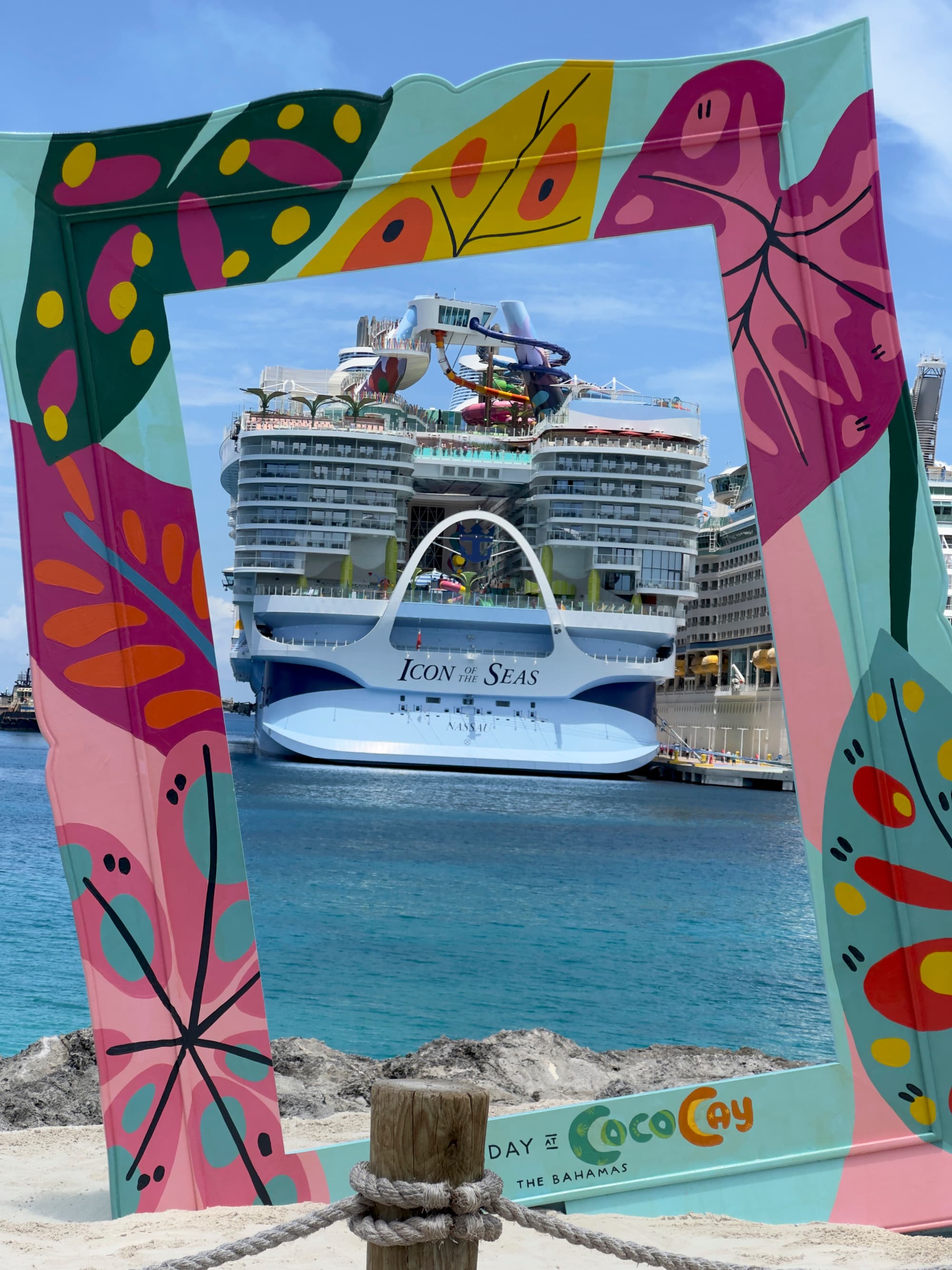 Icon of the Seas docked by a sandy beach on a sunny day.