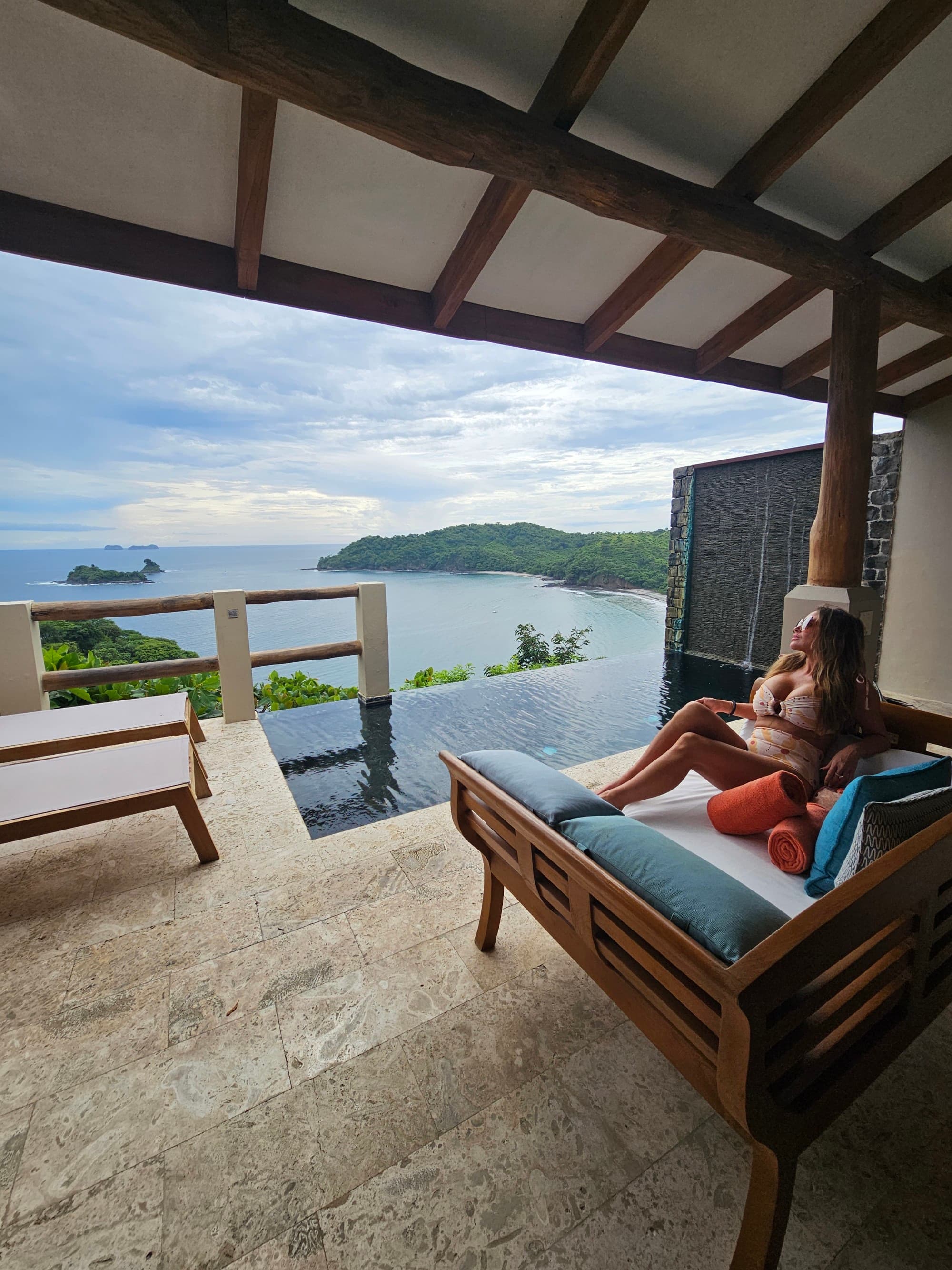 An open-air hotel balcony with a swimming pool and view of the sea during the daytime