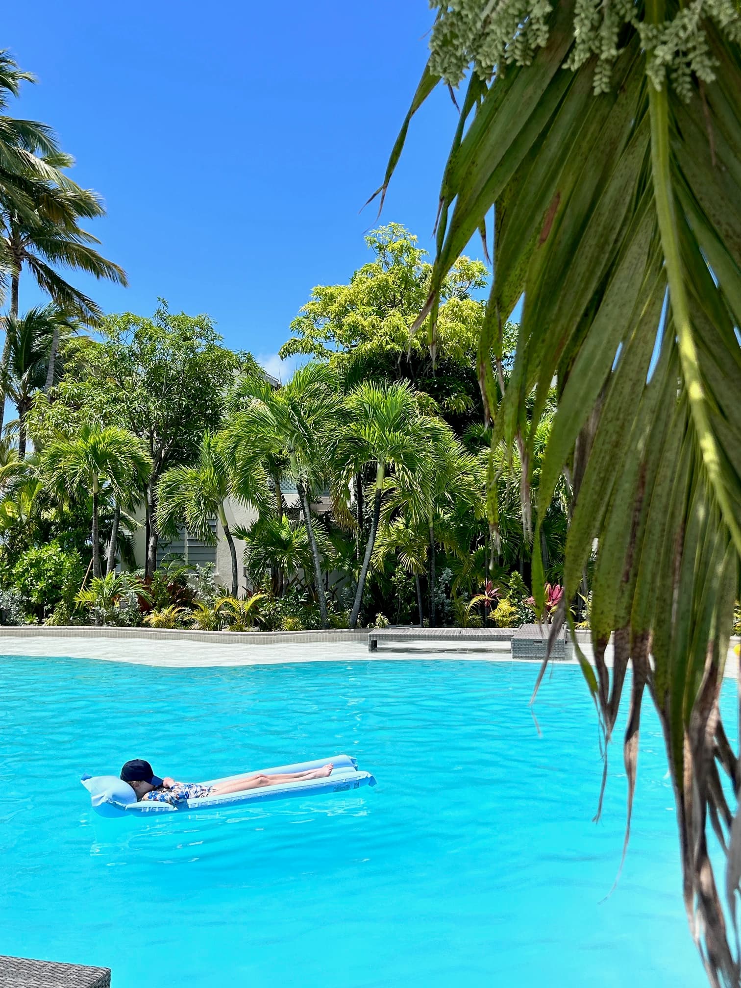 A person laying on a water bed in an outdoor swimming pool surrounded by trees