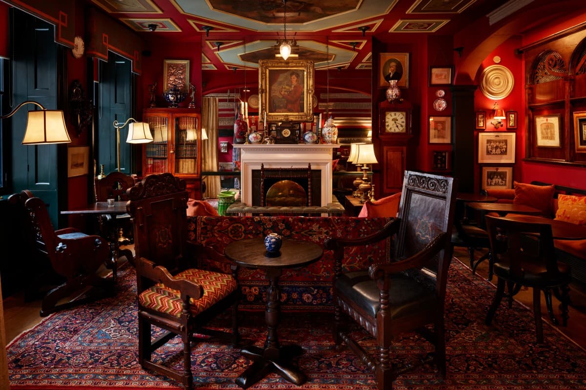 a handsome British lounge with red walls covered in paintings