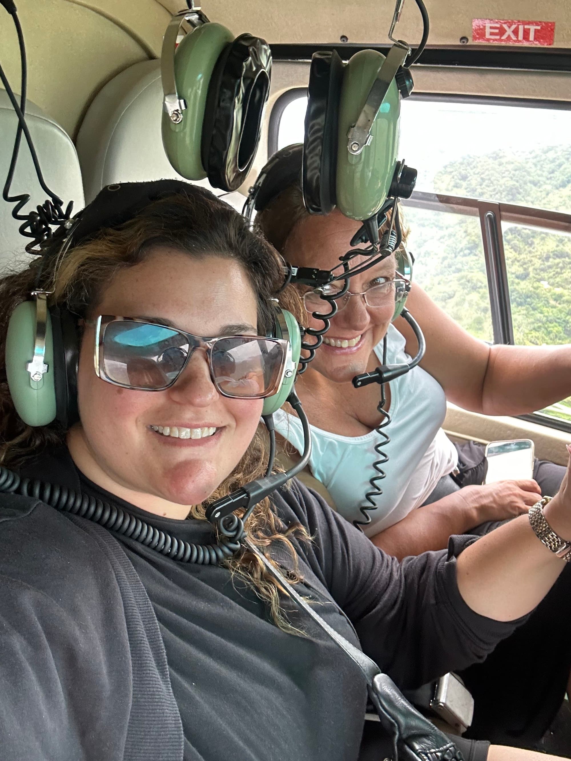 Two people wearing headsets inside a helicopter smiling for a selfie photo