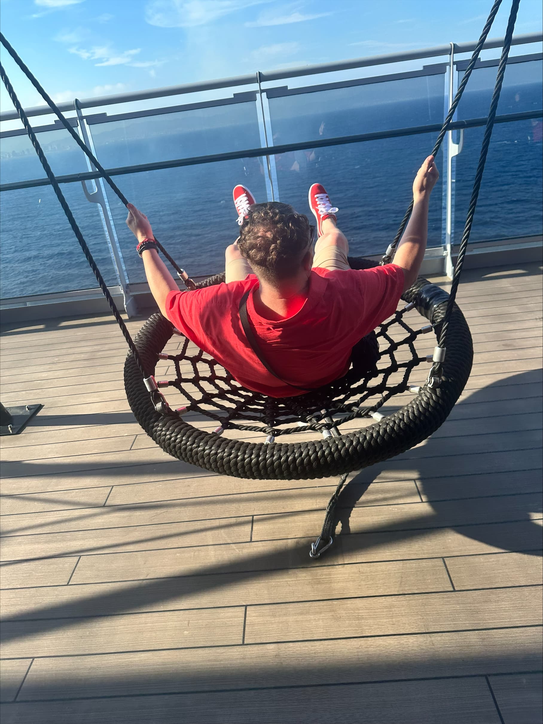A person on a swing on a balcony looking out onto a view of the water