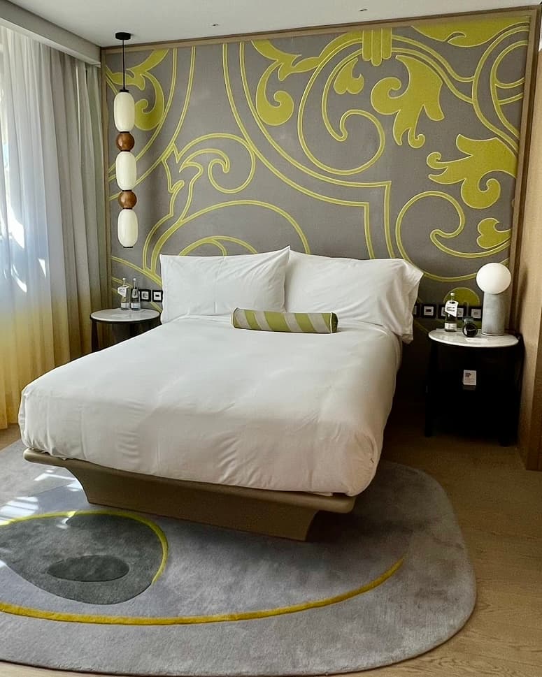 A hotel room at the W Hotel with white bedding and patterened yellow and gray wallpaper behind.