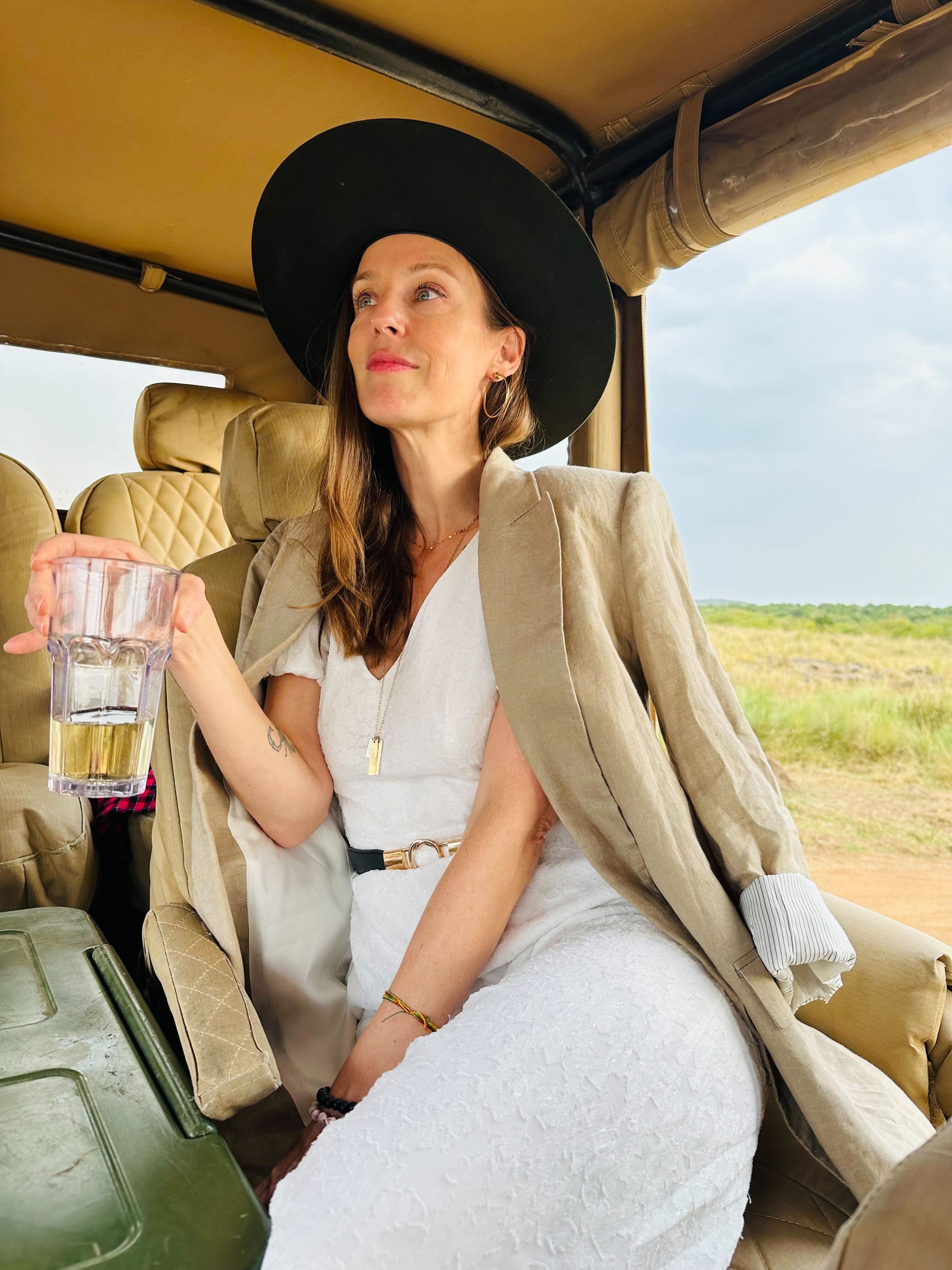 a woman in a black hat and a tan blazer sits in a safari truck