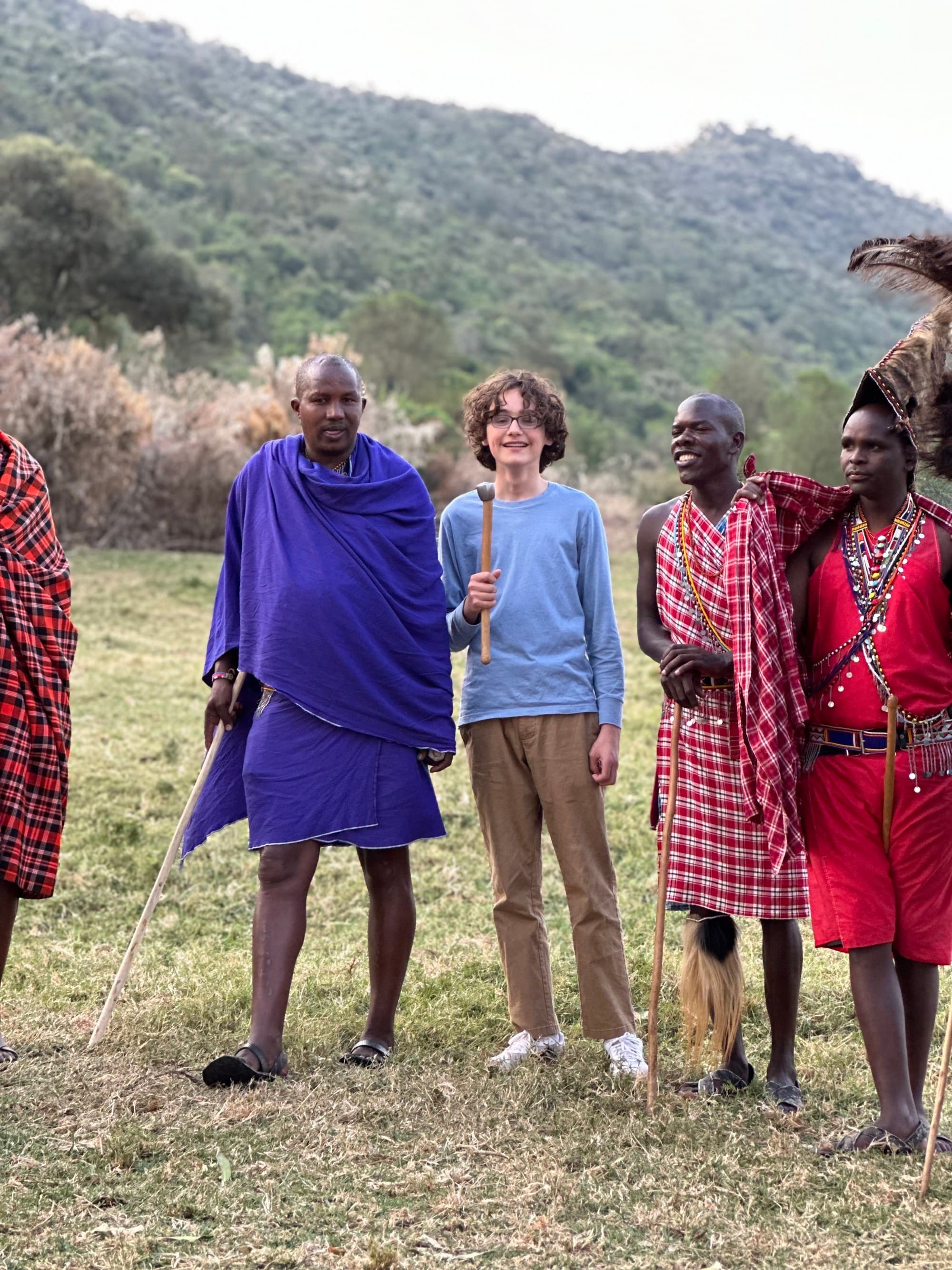 a young man stand amid a group of Maasai people clad in red garments