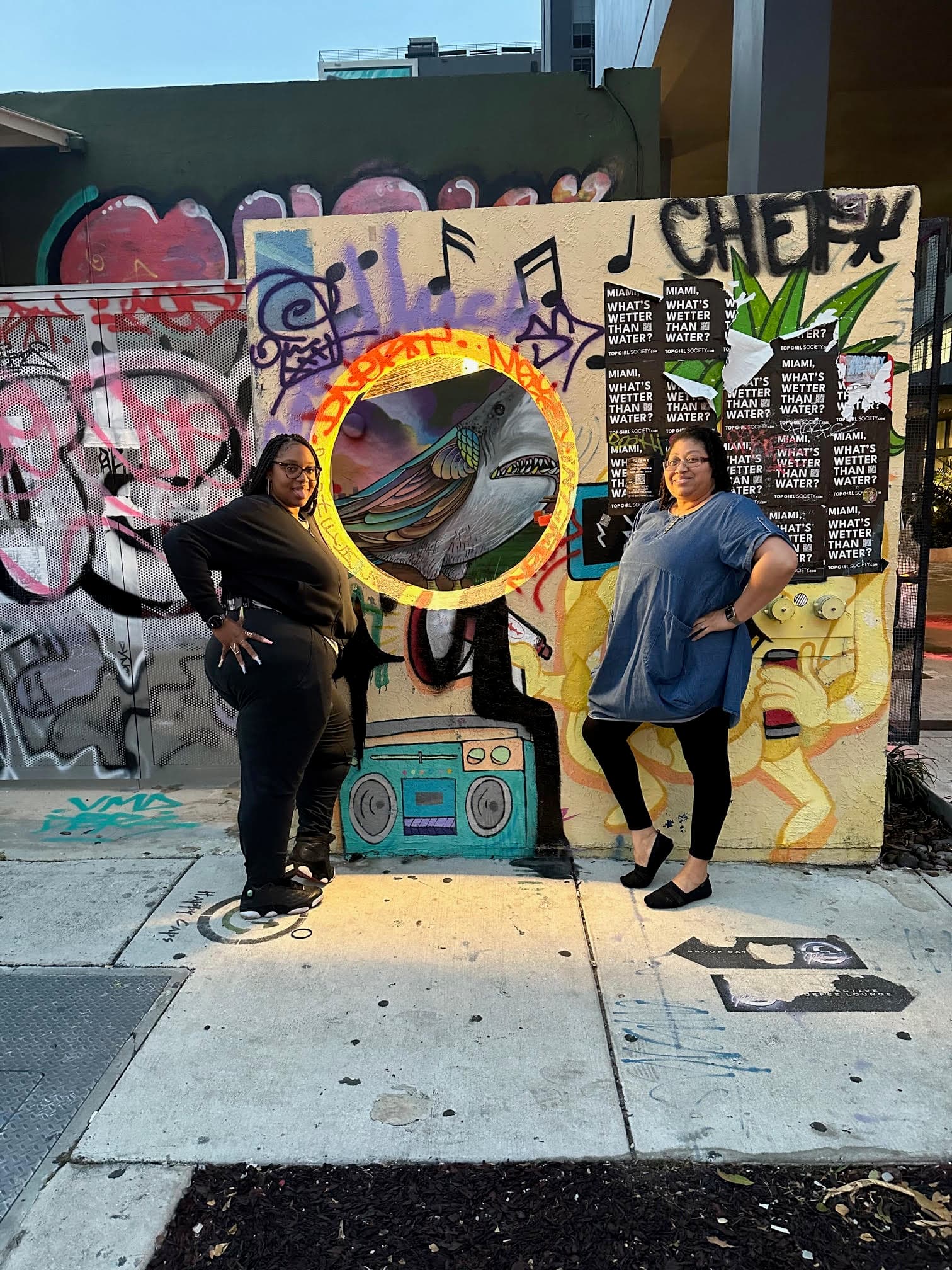 Two people posing for a photo in the street next to a wall art mural