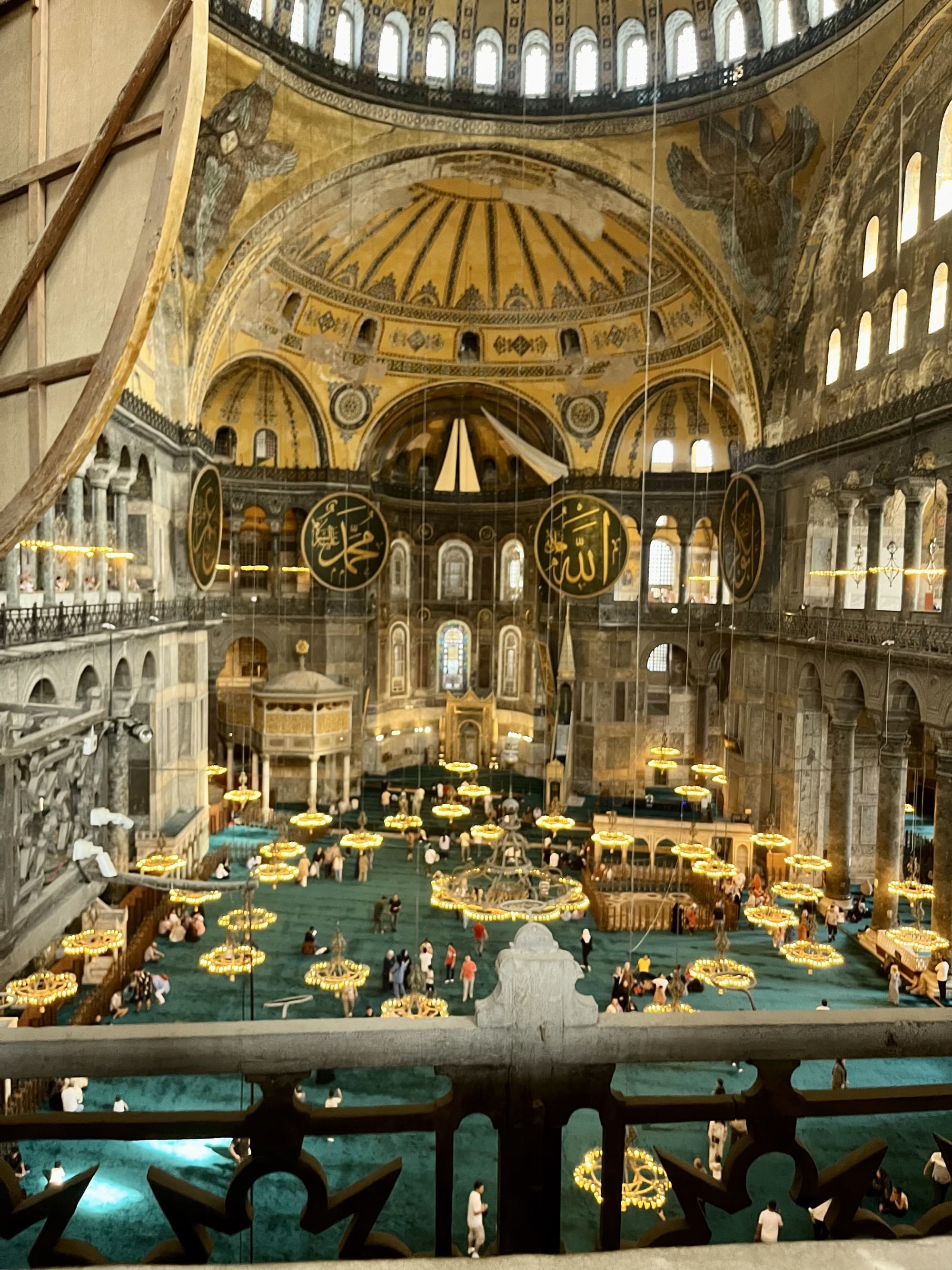 Inside the Hagia Sophia with gold interiors, a large dome-shaped ceiling and hanging gold lights.