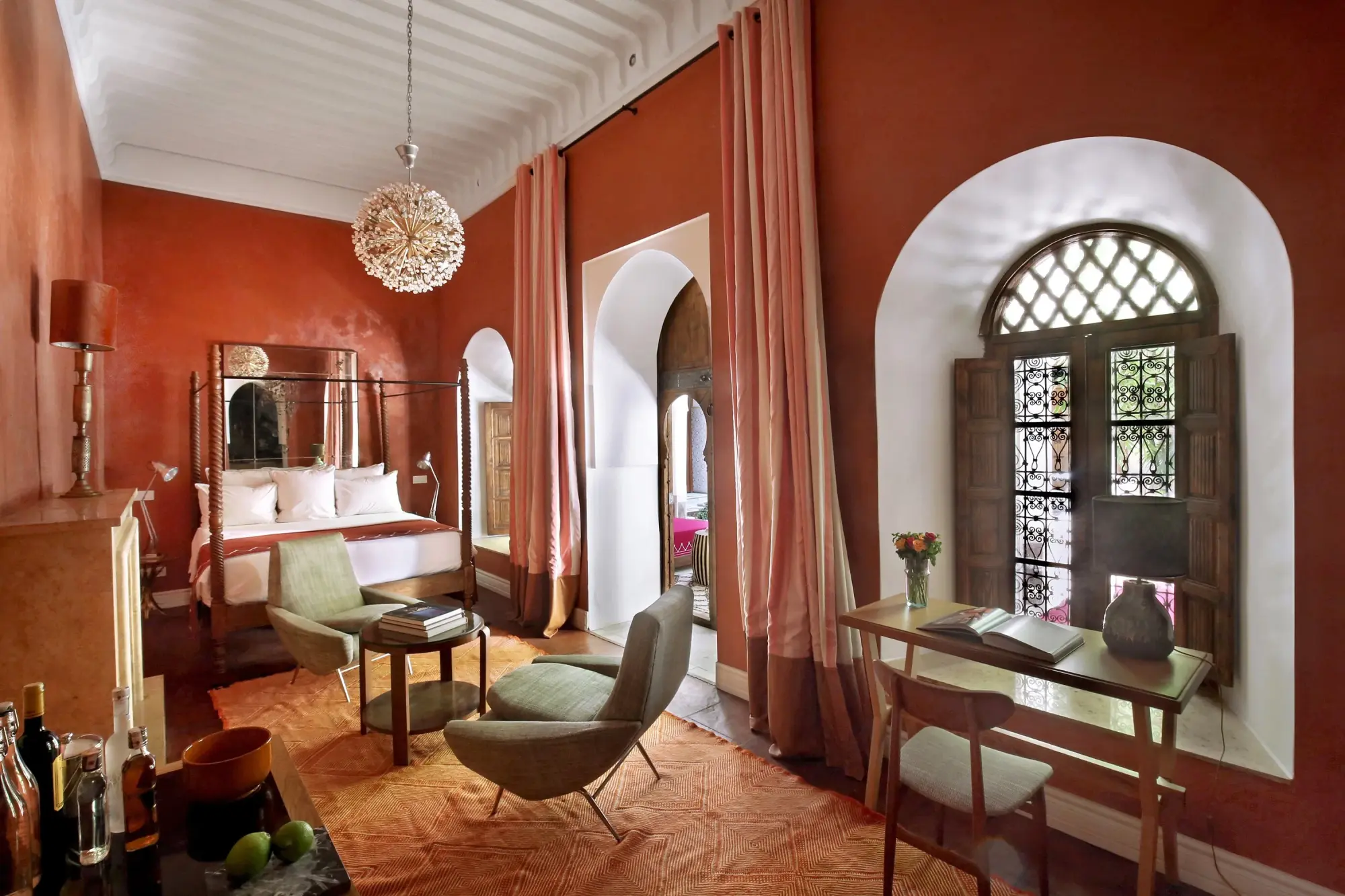 a luxe Moroccan hotel room with orange-pink walls and a modern floral chandelier
