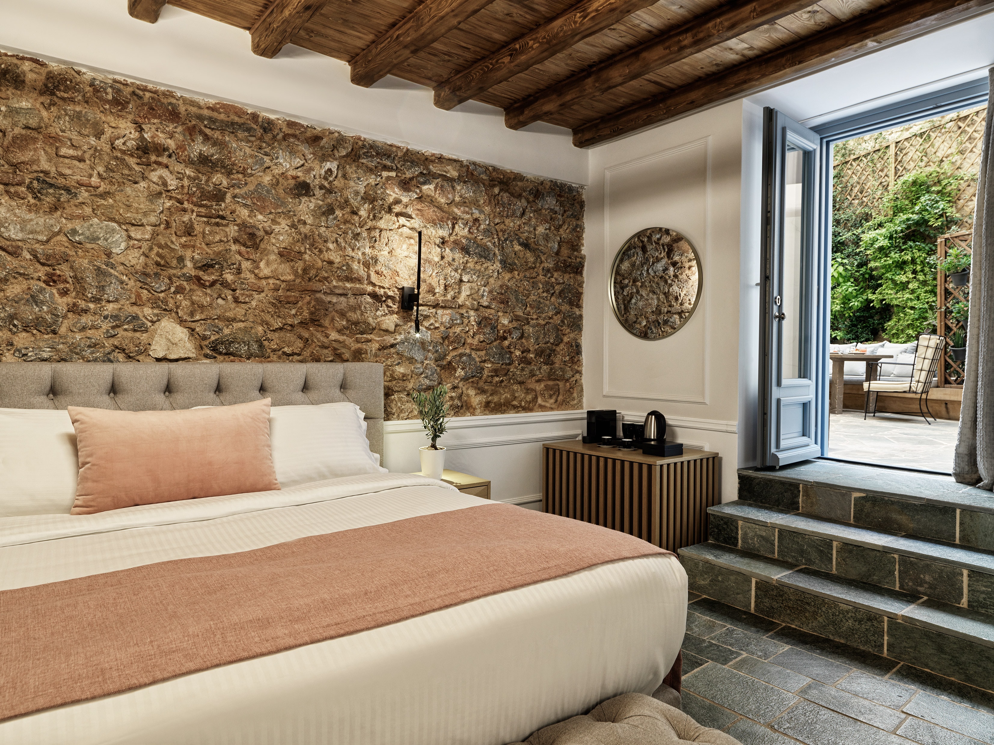 A room at A77 suites with a stone wall feature, large bed, beamed ceiling and steps leading out to a patio.