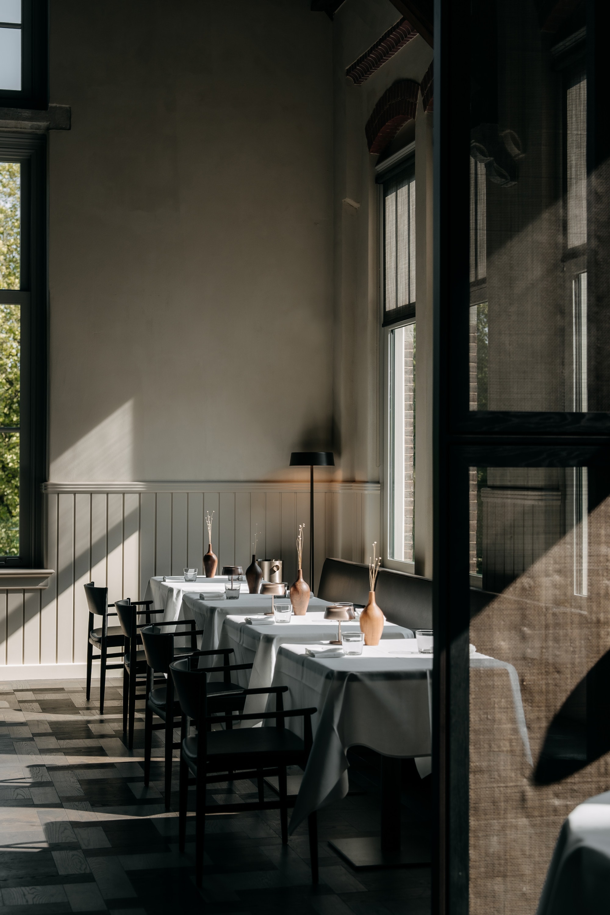 An elegant restaurant with white tablecloths and black chairs. The room has a high ceiling and lots of natural light.