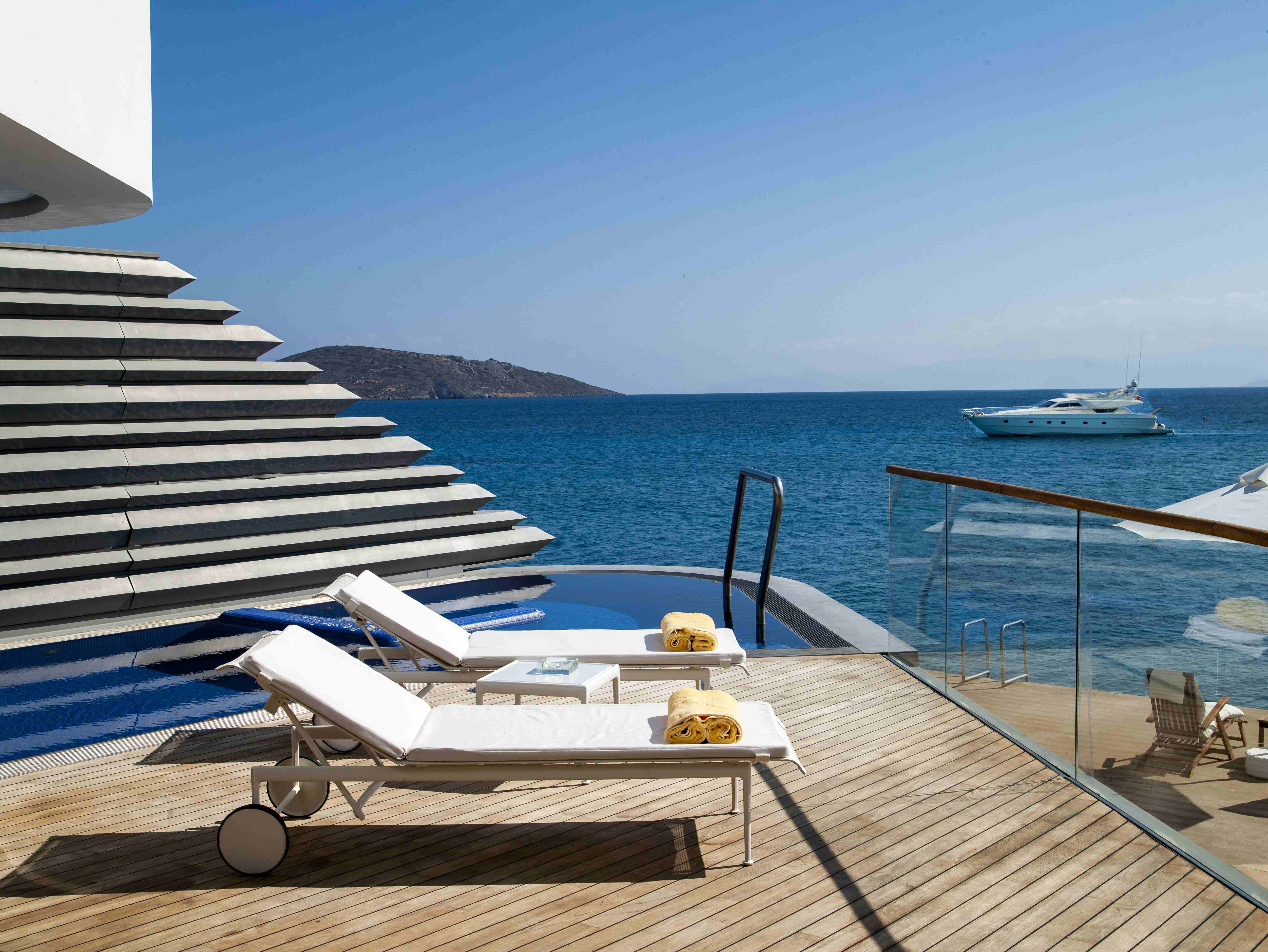 A view of a deck with sun loungers and a glass balcony, private pool and ocean views.