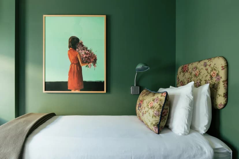 small white bed in a green room with a painting of a young girl