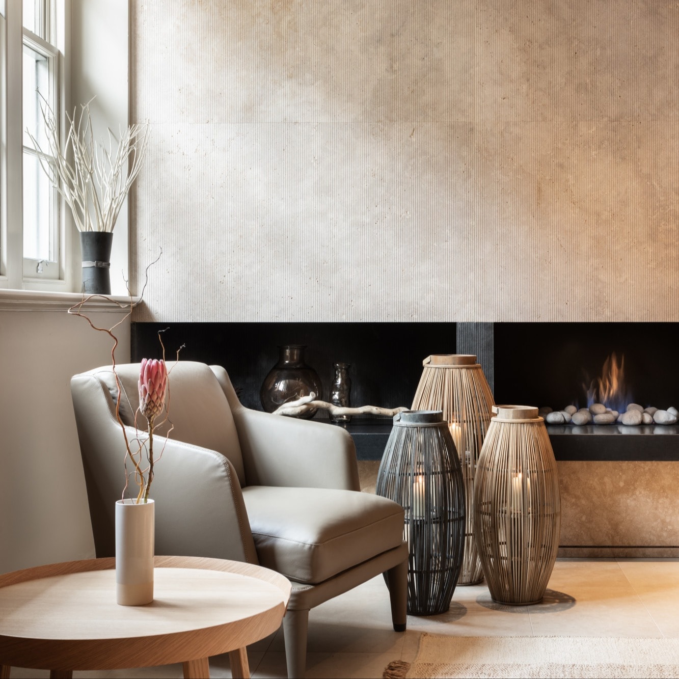 a gray arm chair rests besides a trio of oval pots near a modern black fire place