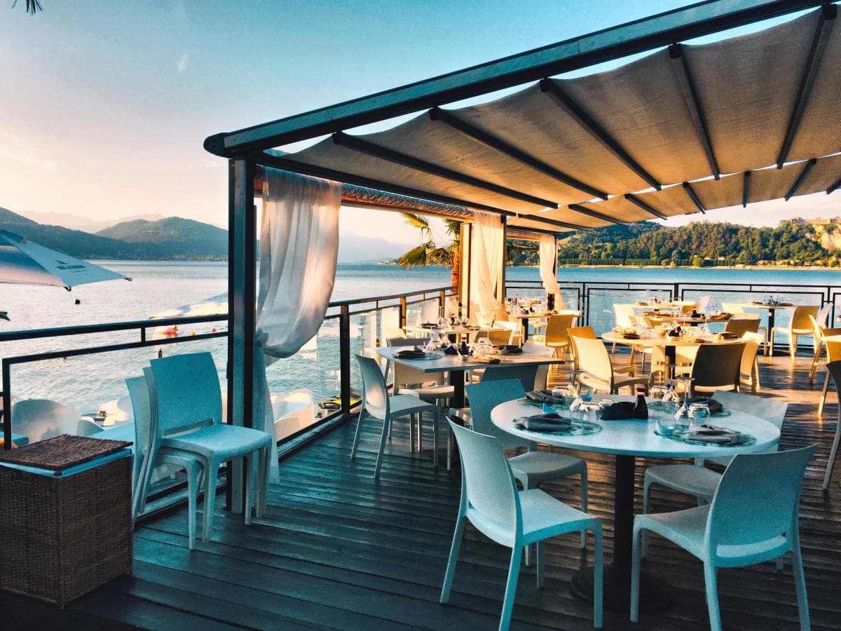 White tables and chairs on a wooden deck at a restaurant overlooking the water and mountains