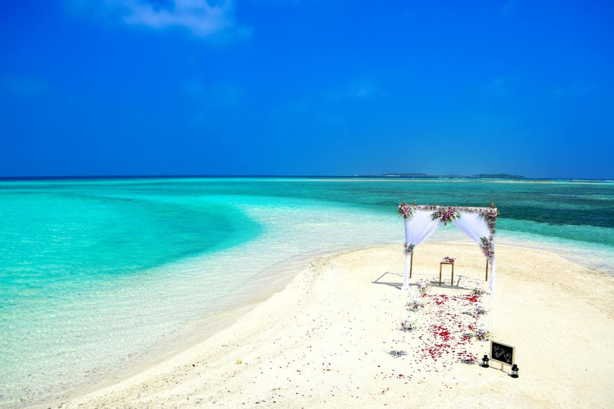 Alter with pink flowers on private white sand beach surrounded by turquoise waters with a bright blue sky
