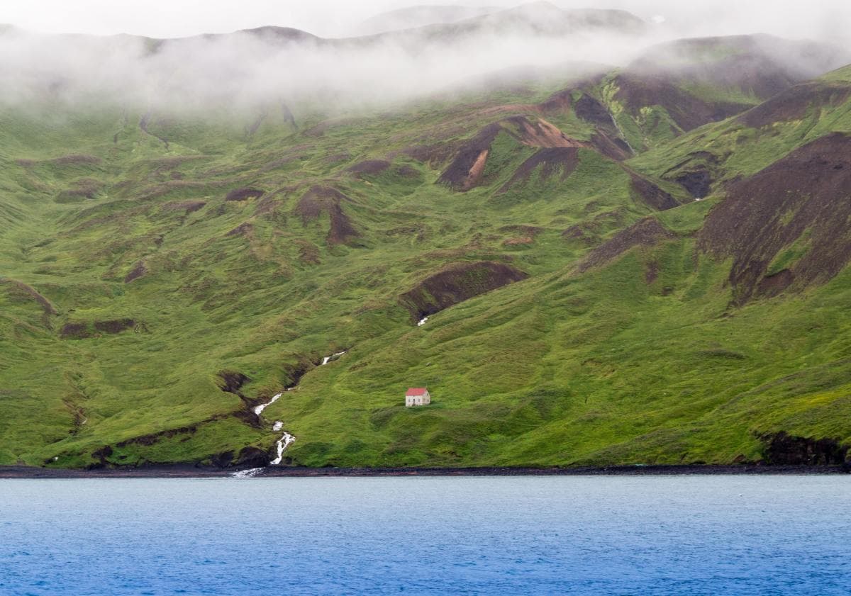 Mysterious house on green mountain pastures next to the ocean on a foggy day in Iceland.