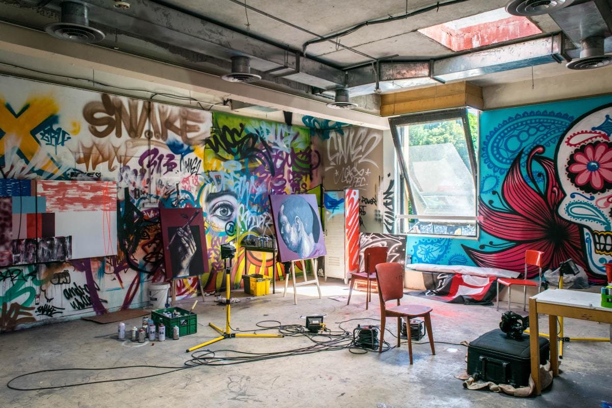 Inside gallery and open-space studio of street artist in France with colorful graffiti on walls and paintings displayed on easels.