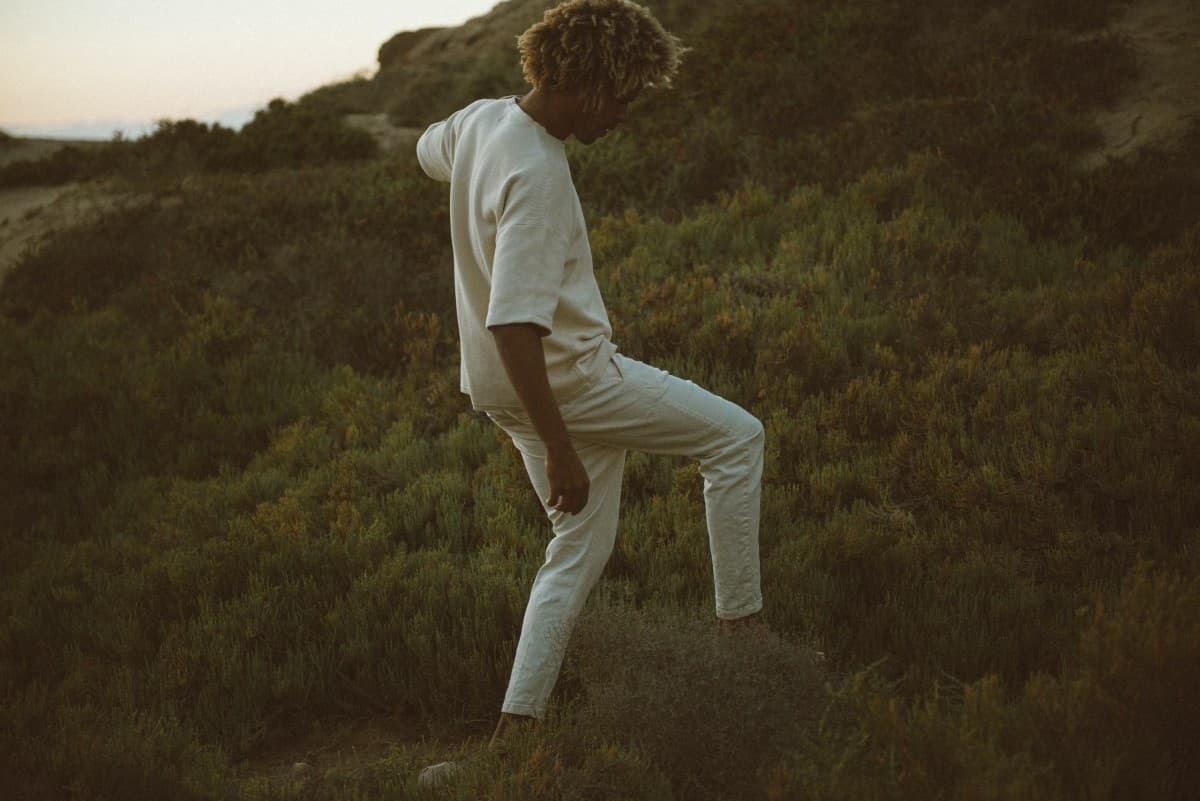 Man walks up an unpaved hill through grass and shrubs.