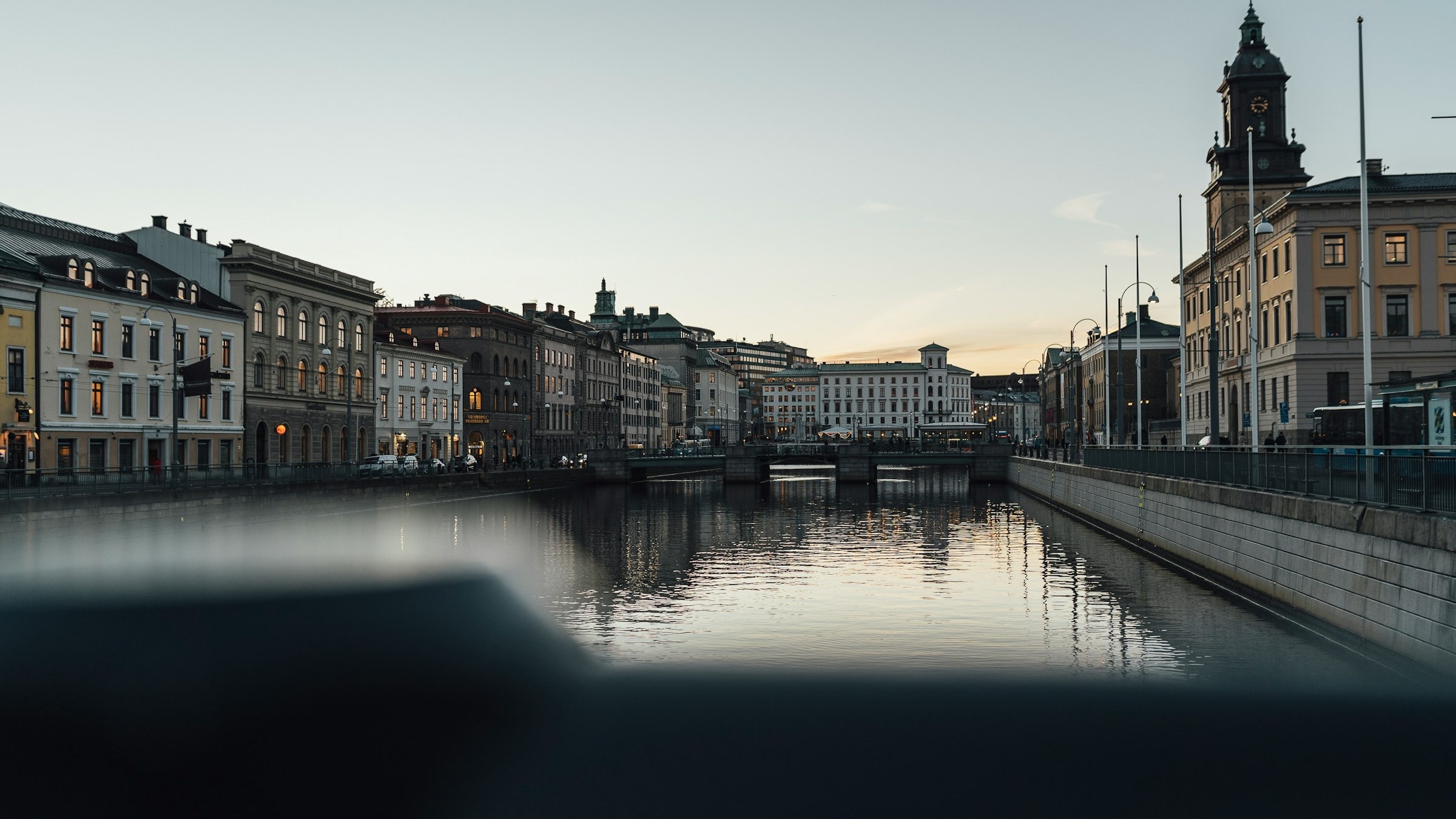A view from the river with buildings either side taken in a city in dim evening light