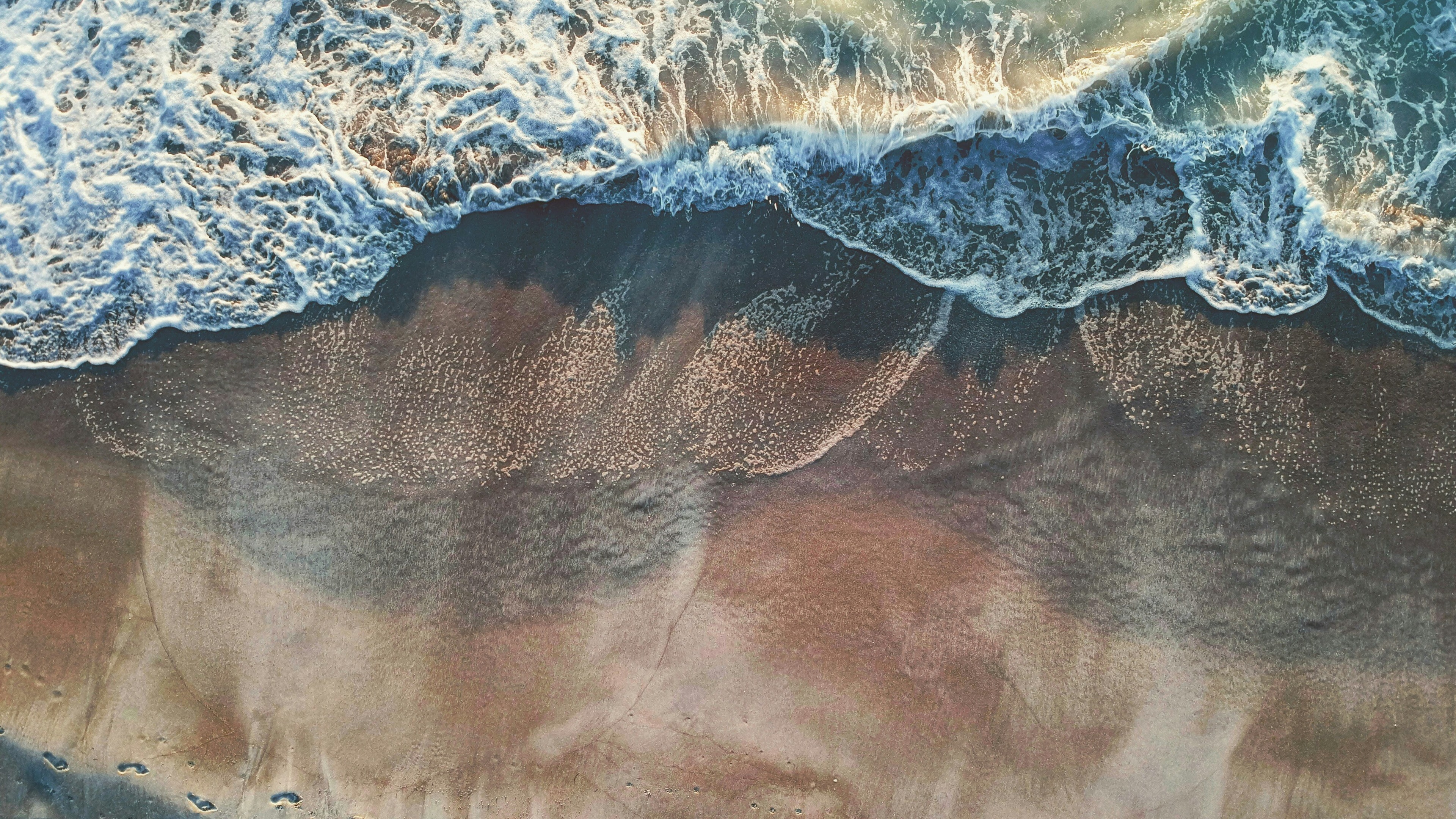 An aerial view of turquoise waves crashing on a pink-hued sandy beach in Sarasota.