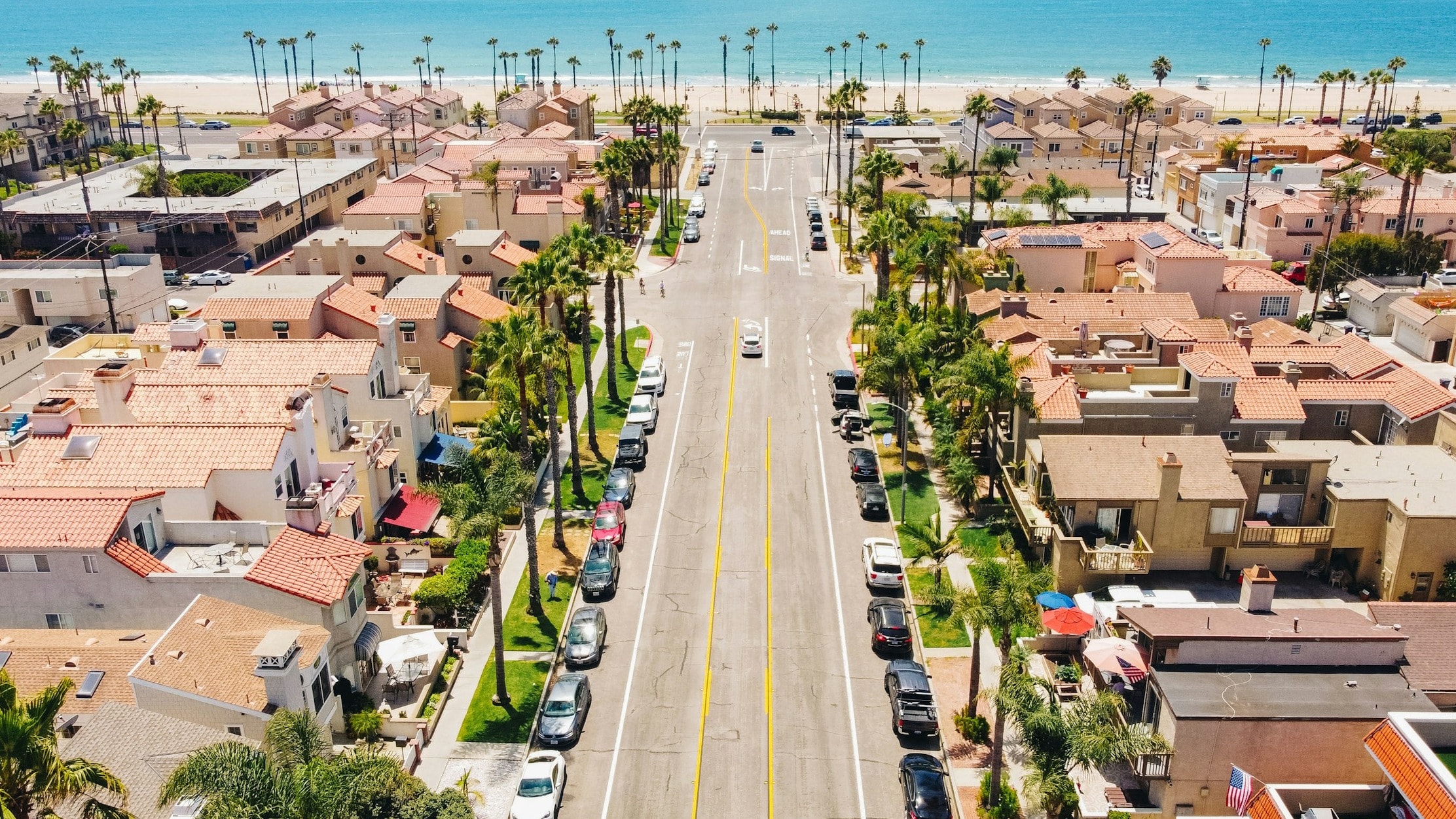 A long street leading down to the beach with buildings either side and cars parked.
