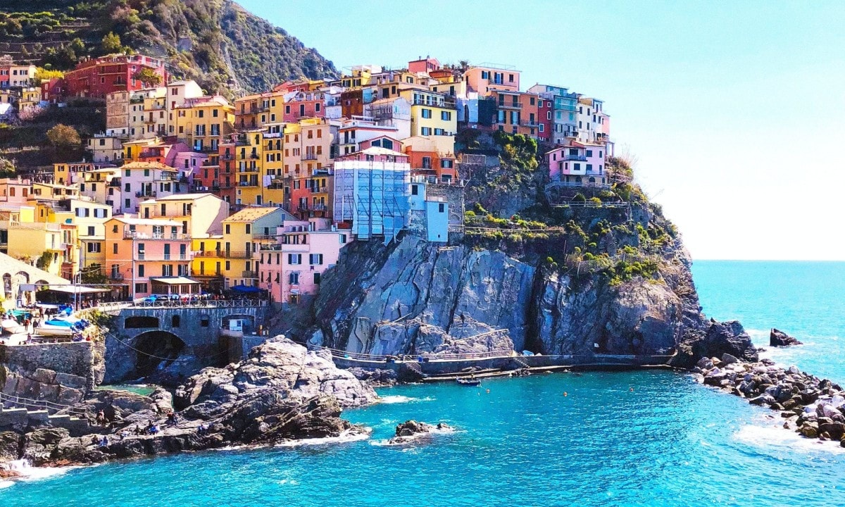 Colorful buildings of Cinque Terre on a cliff over the ocean on a sunny day.