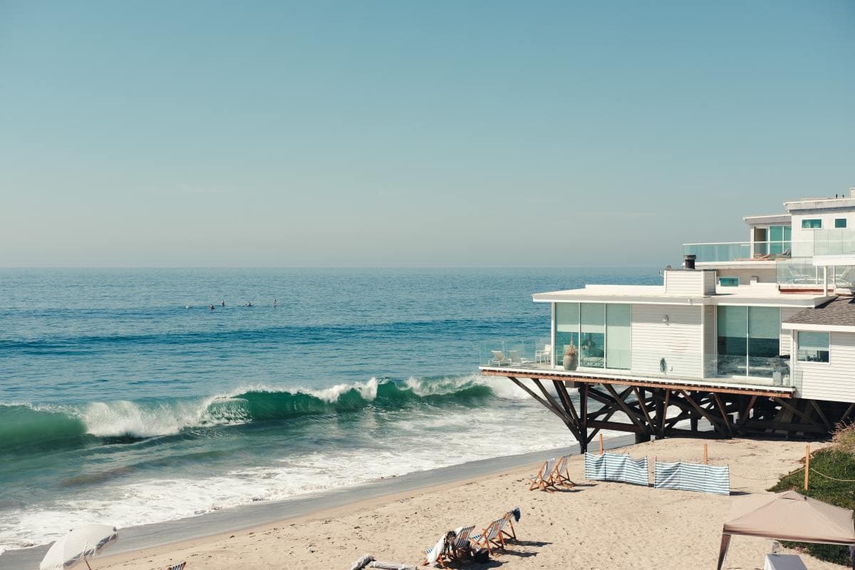 Seaside resort on shore with floor to ceiling windows and lounge chairs on a clear day.