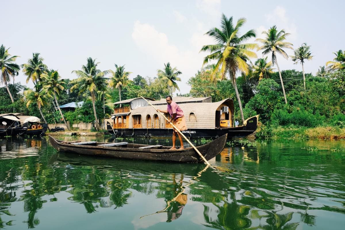 Man rowing boat through a green, jungle river in the backwaters of Kerala, India.
