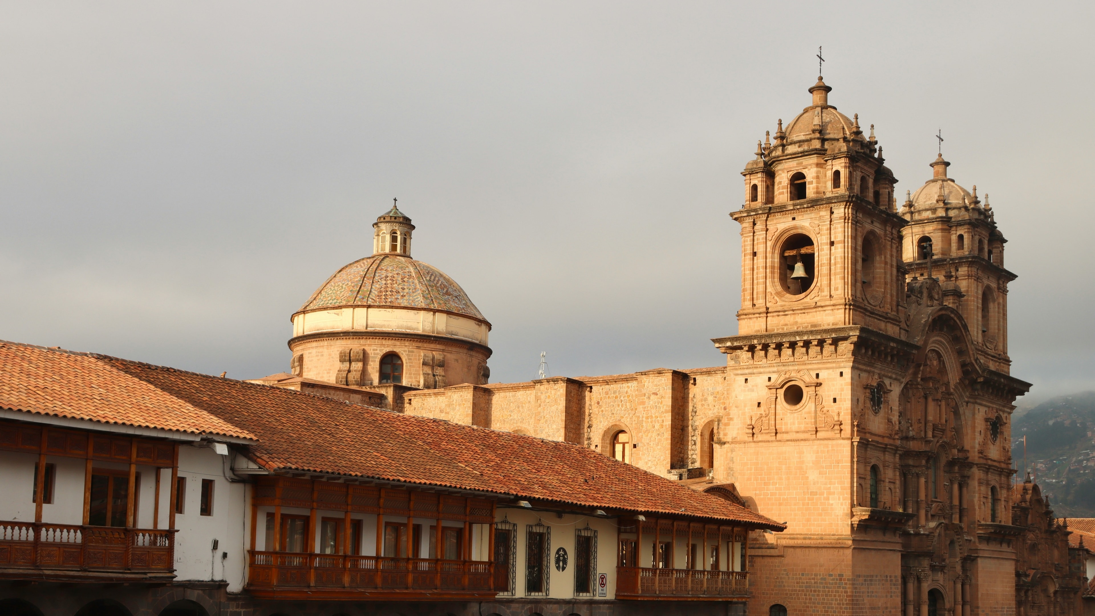 A side view of the Cusco Cathedral towards sunset, with two tall towers next to a lower building.